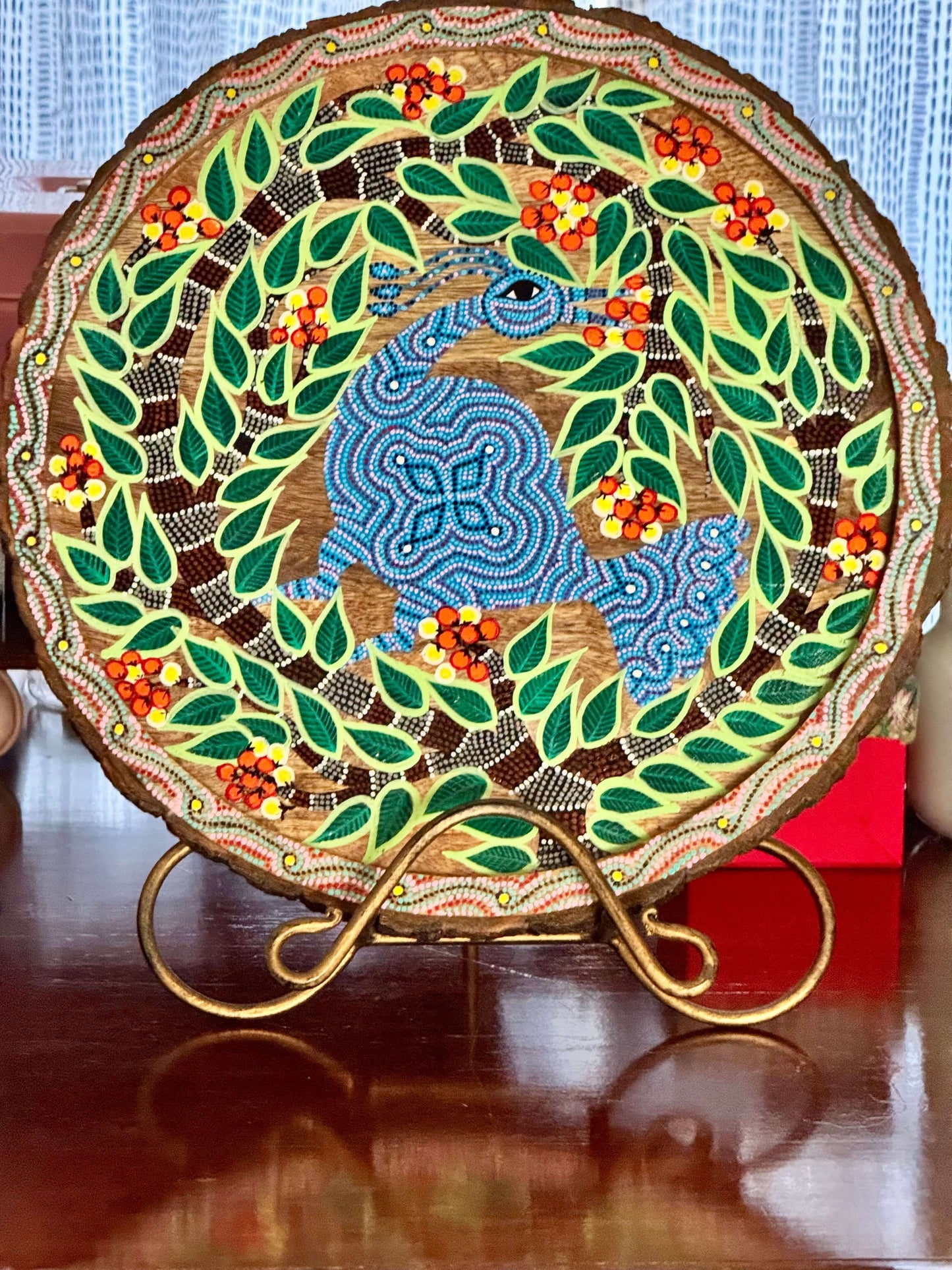 Decorative plate with a Bhil art peacock design surrounded by leaves and berries on a stand.
