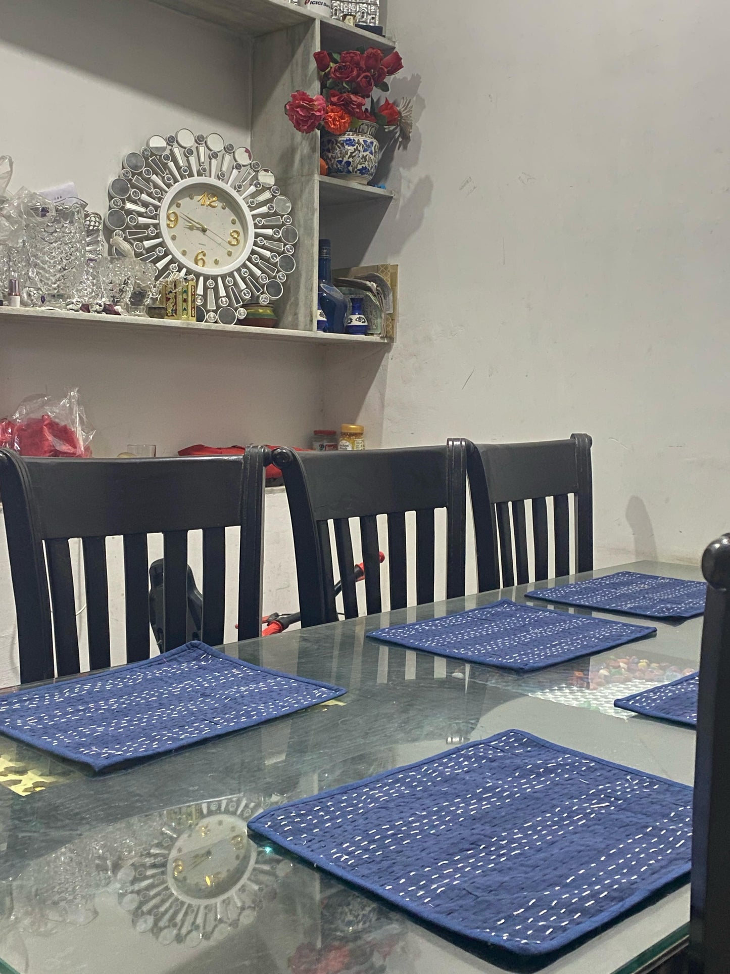 Dining table set with reversible blue Kantha placemats and chairs in a room with shelves and decorative items.