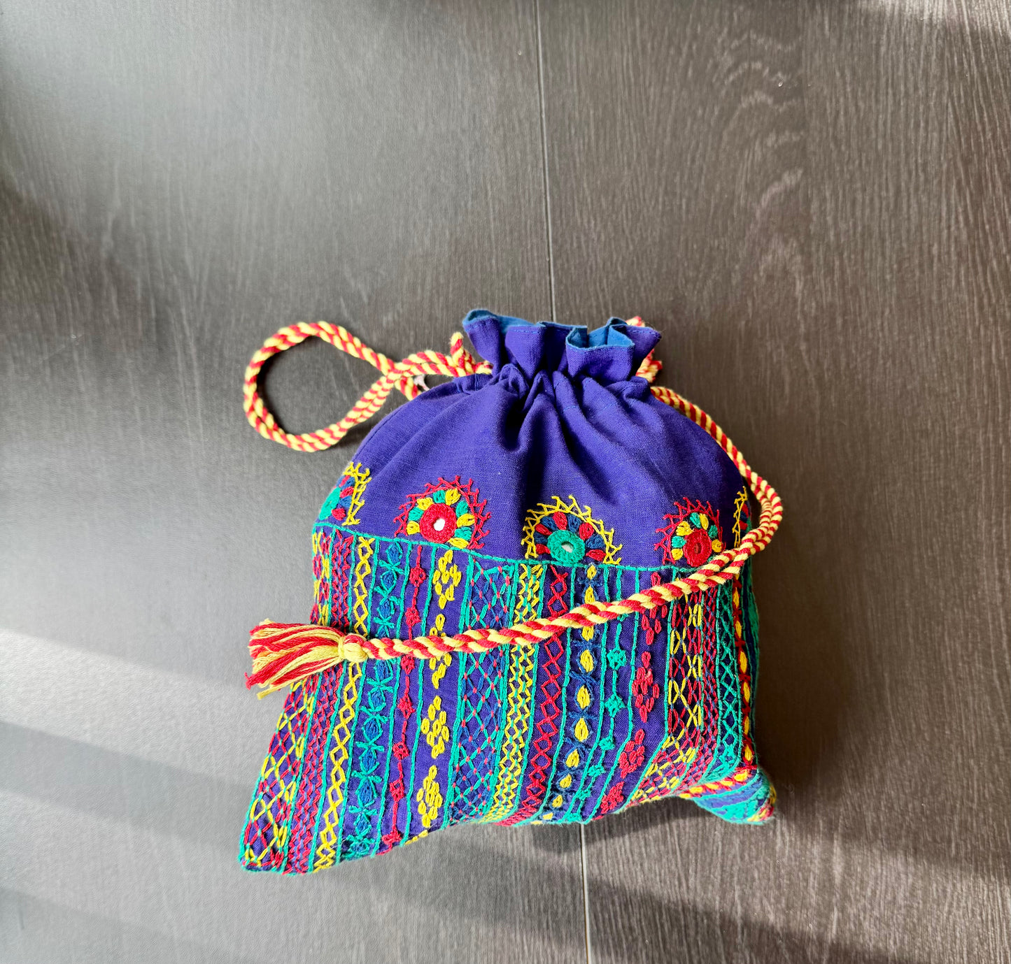 A traditional Lambani embroidery art potli bag with red, green, and beige colors, featuring geometric patterns and a drawstring closure.
