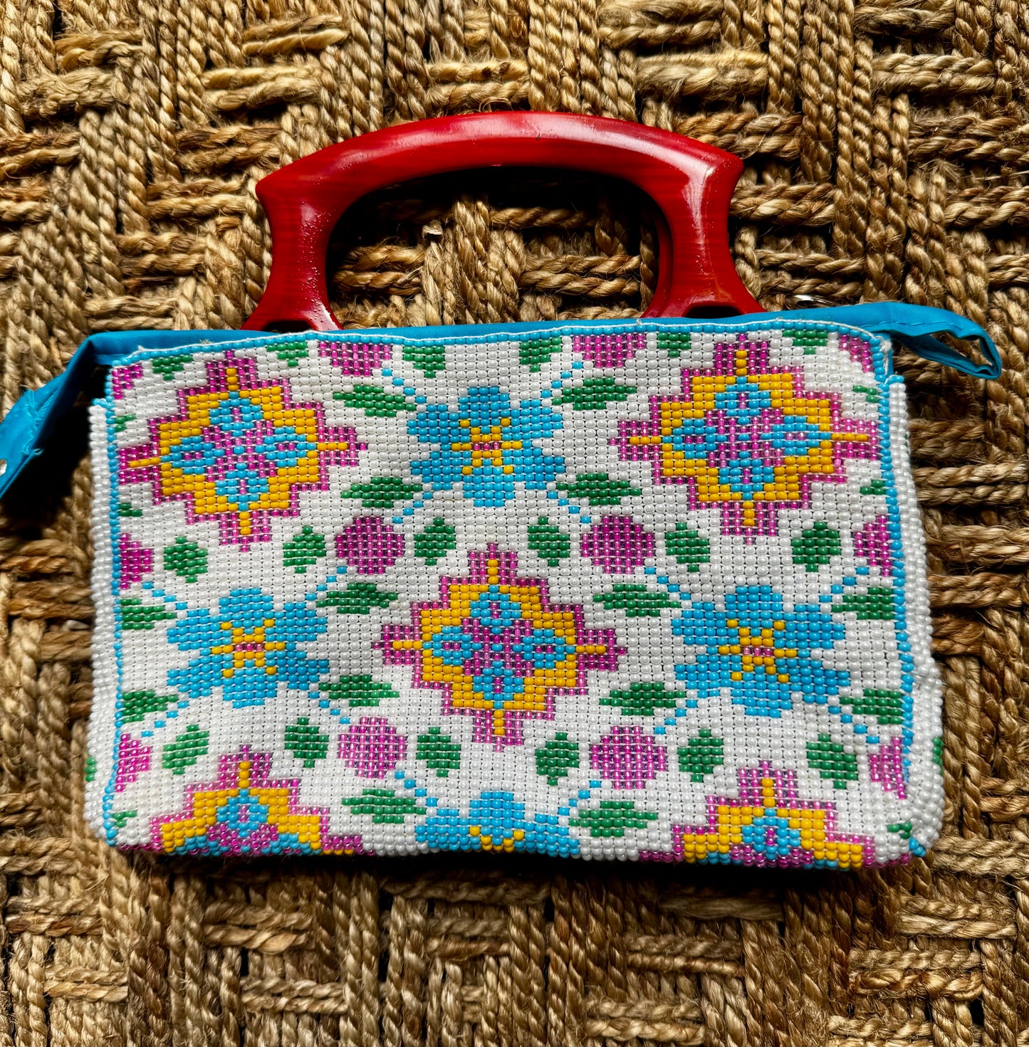 Decorative Motikaam - strung Pearl work handbag clutch with colorful design on a textured fabric background Handmade cross-stitched bag with colorful floral patterns on a woven surface