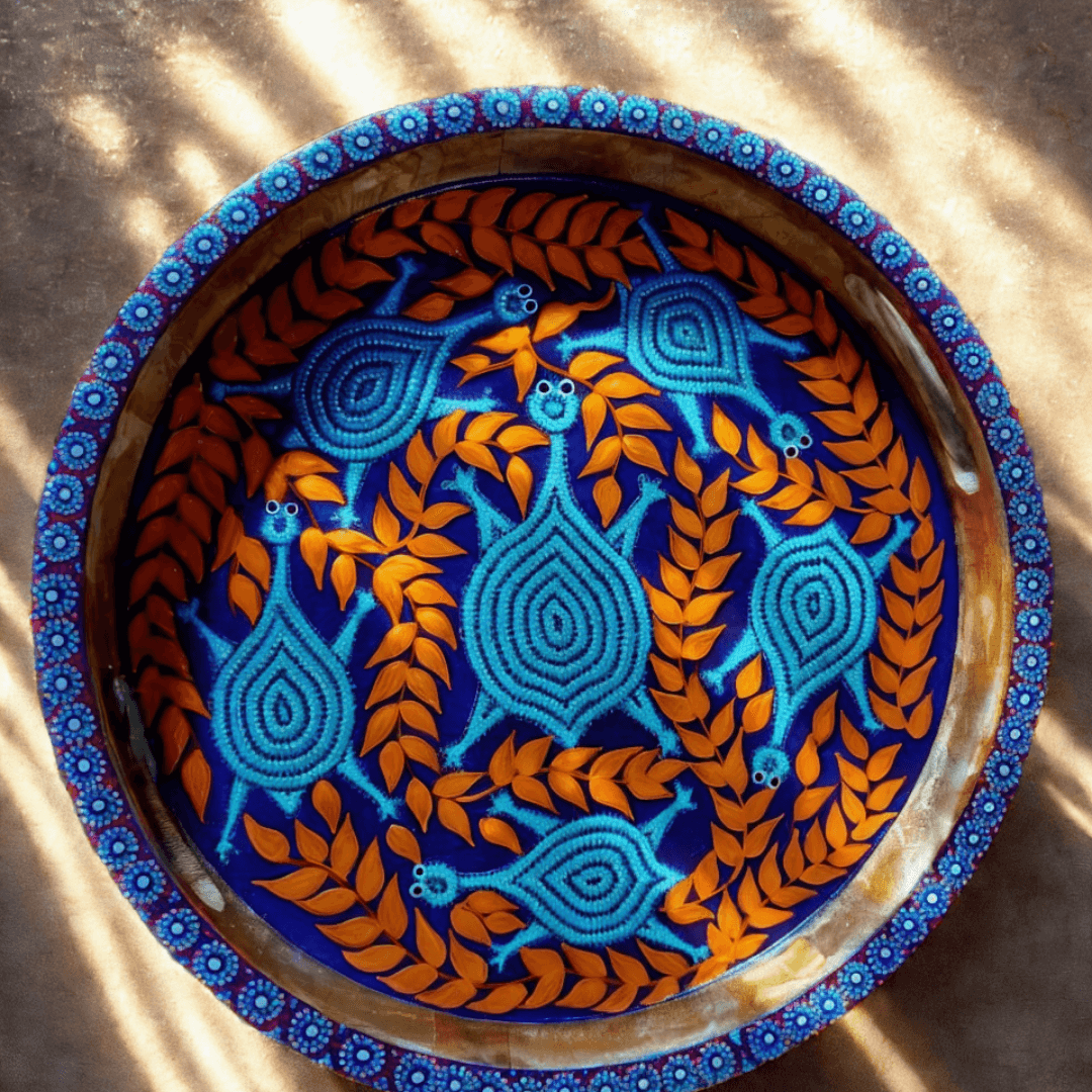 Decorative Bhil art tray/plate with blue and orange patterns on a textured surface