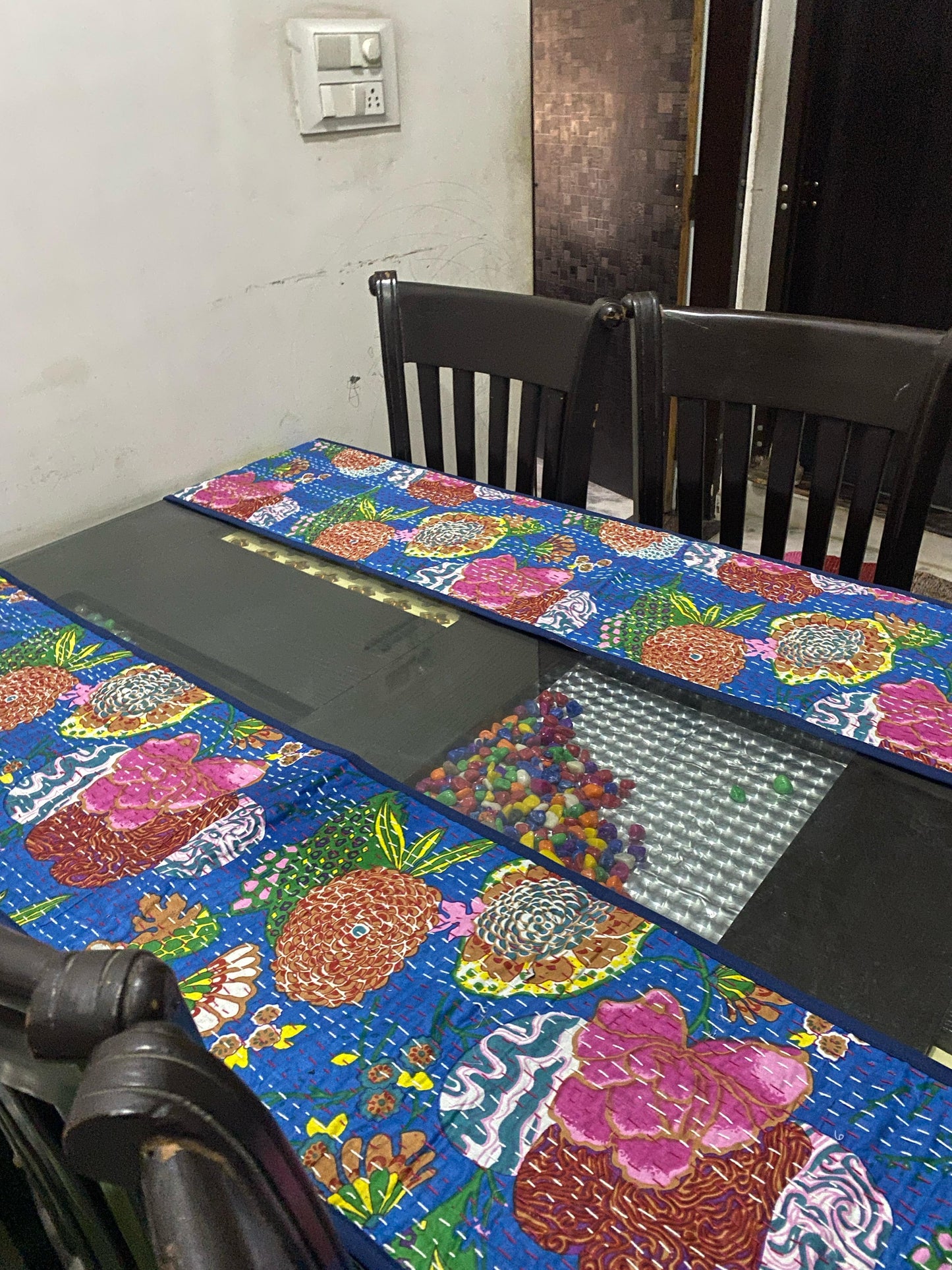 Dining table with a colorful tablecloth and chairs in a room.