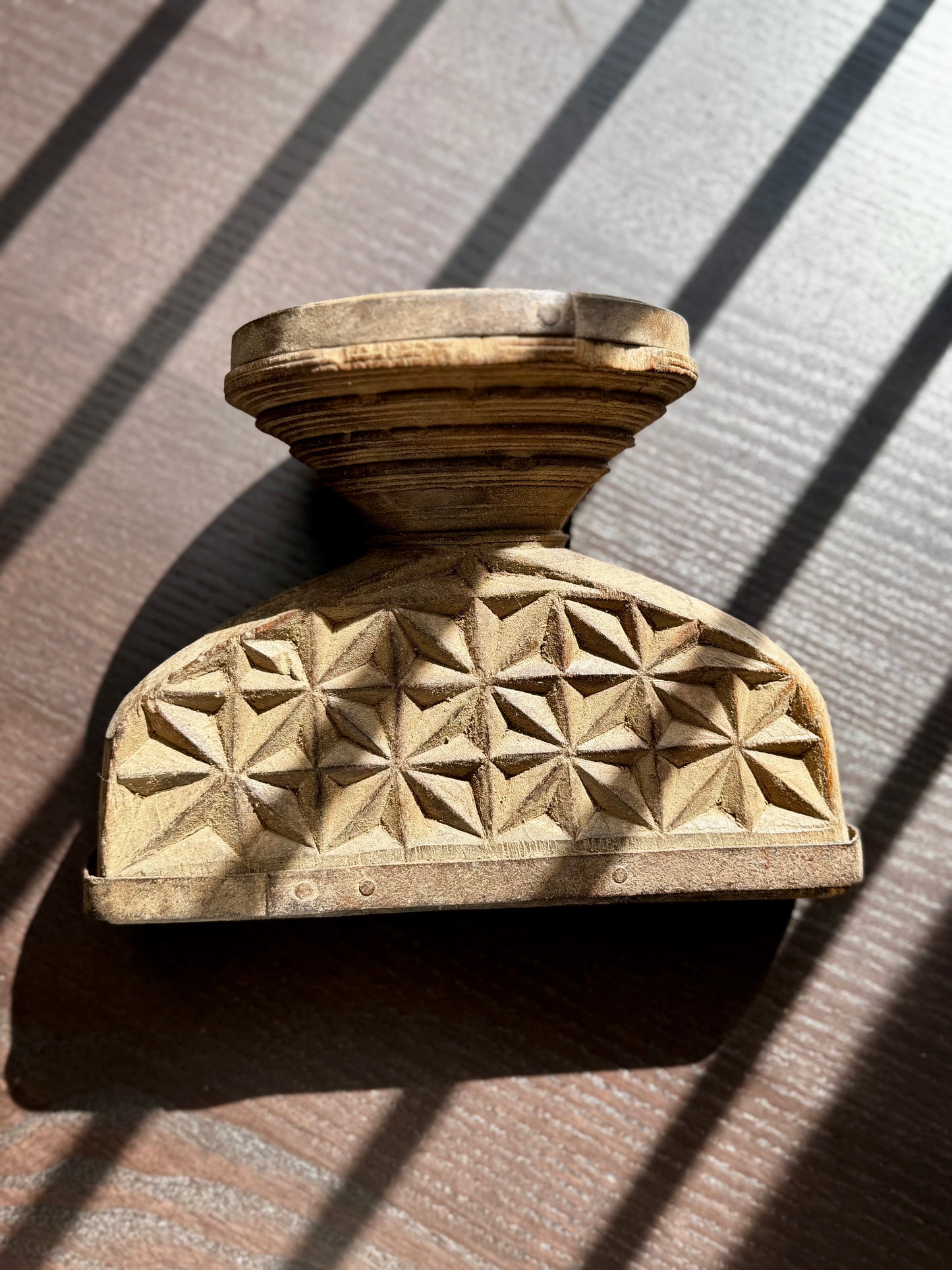 Wooden candle holder on its side with geometric pattern on a textured surface