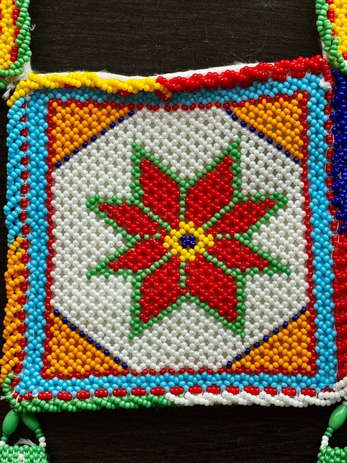 Close up of Colorful Motikaam, strung pearls art design with a red flower-like pattern on a black background