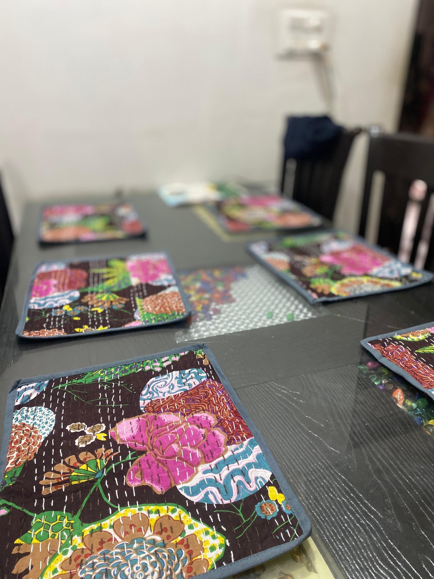 Colorful gray Kantha work patterned placemats on a dining table with a blurred background