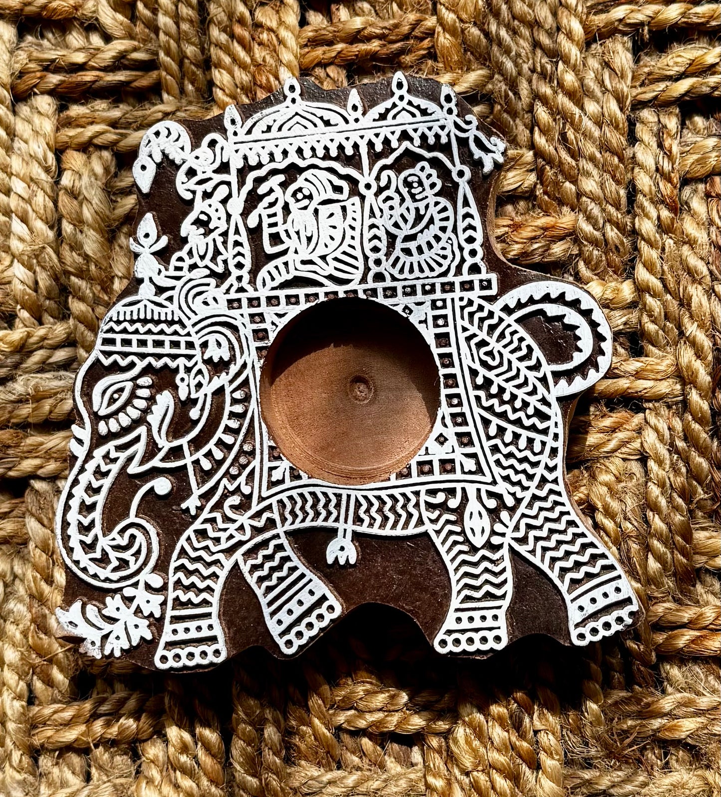 Decorative hand engraved wooden block tea light holder in elephant shape with intricate white patterns on a textured brown background
