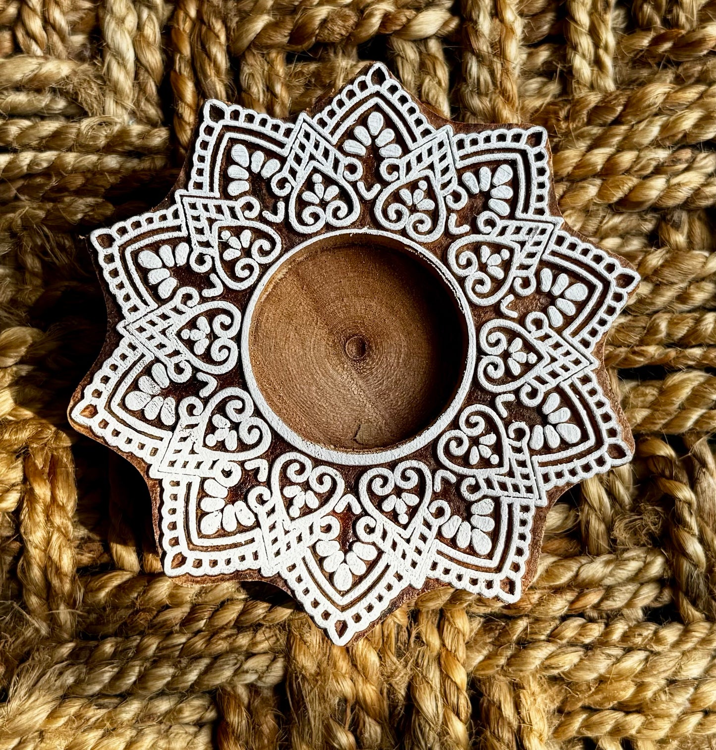 Decorative hand engraved wooden block candle holder with intricate patterns on a woven background