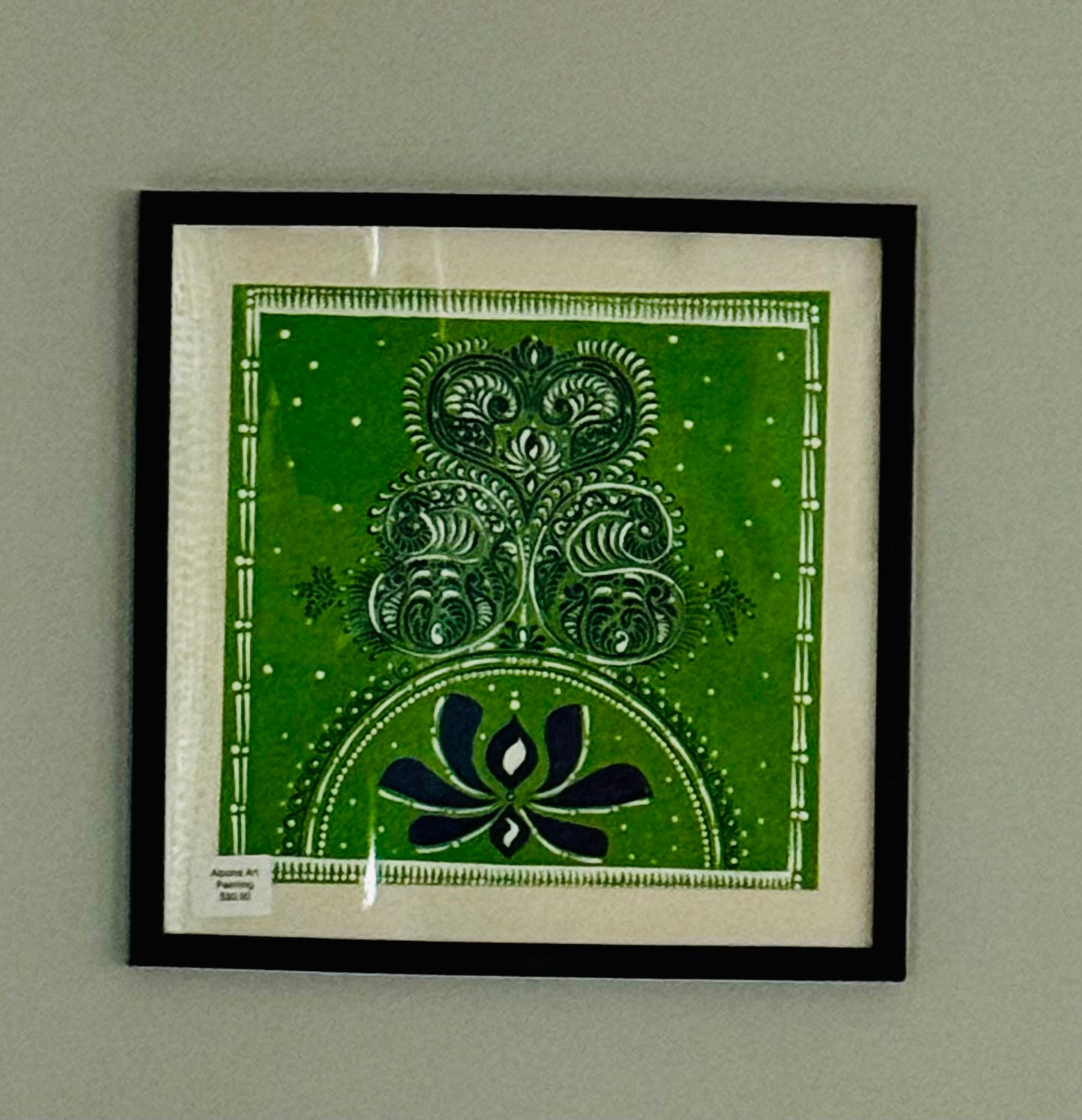 Framed Alpona artwork with a green and black design on a gray wall