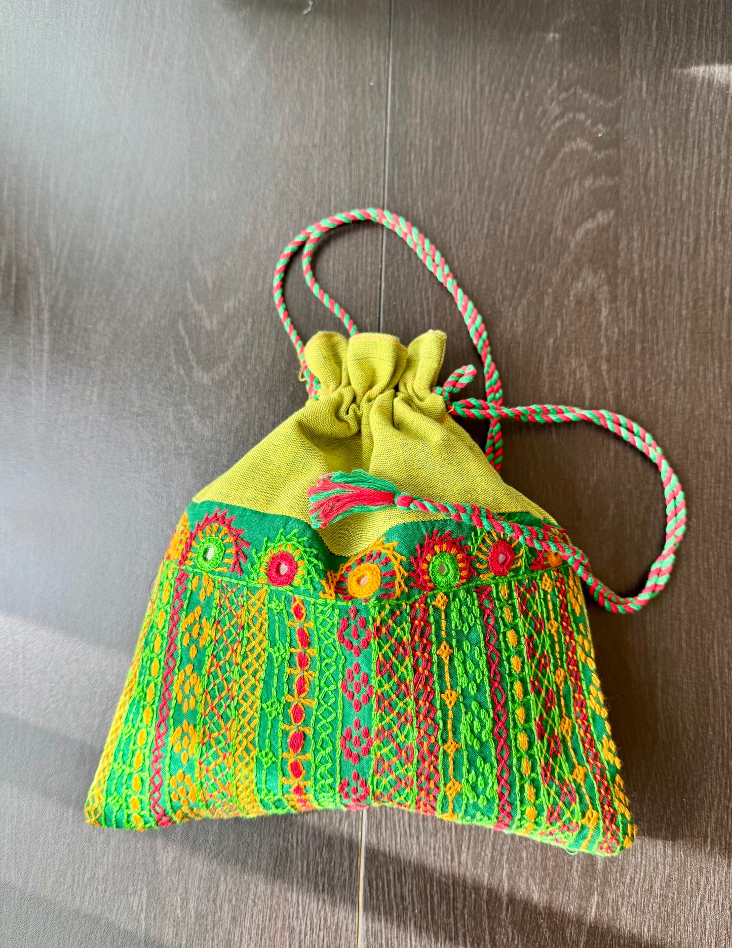 A red Lambani embroidery artesian potli bag with colorful geometric patterns and decorative elements.