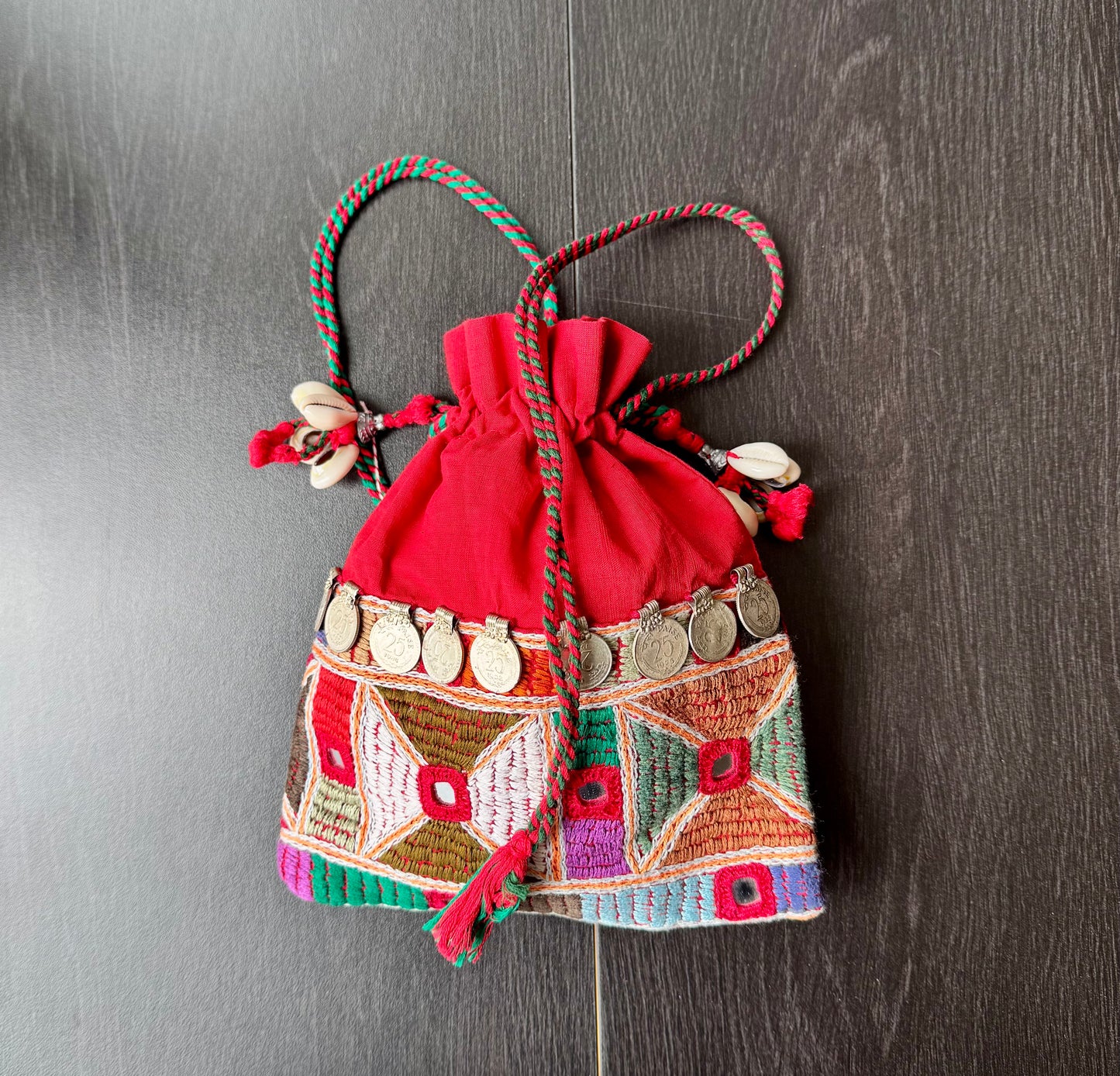 A traditional Lambani embroidery art potli bag with red, green, and beige colors, featuring geometric patterns and a drawstring closure.