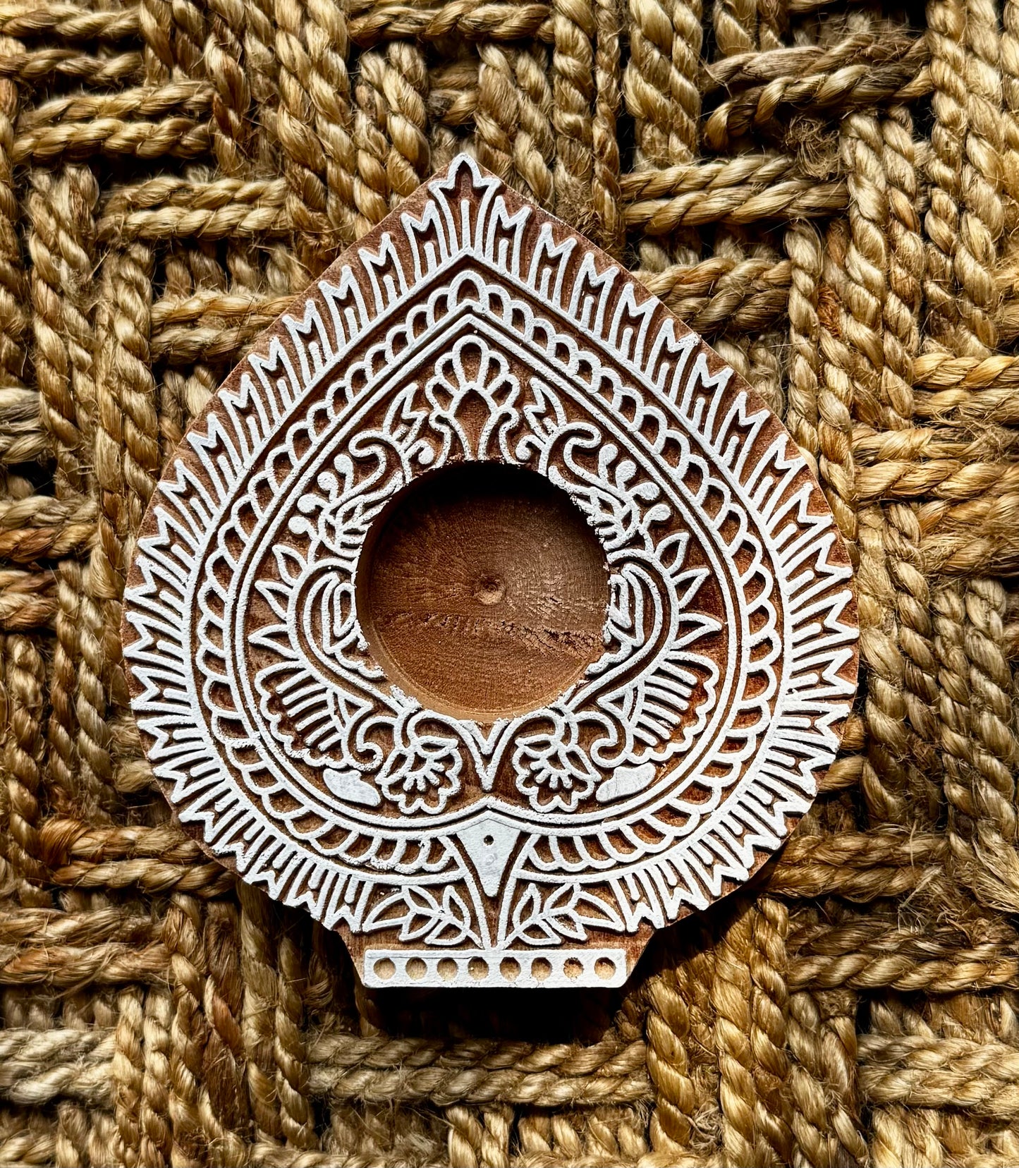 Decorative hand engraved wooden block tea light holder in leaf shape with intricate patterns on a textured woven background