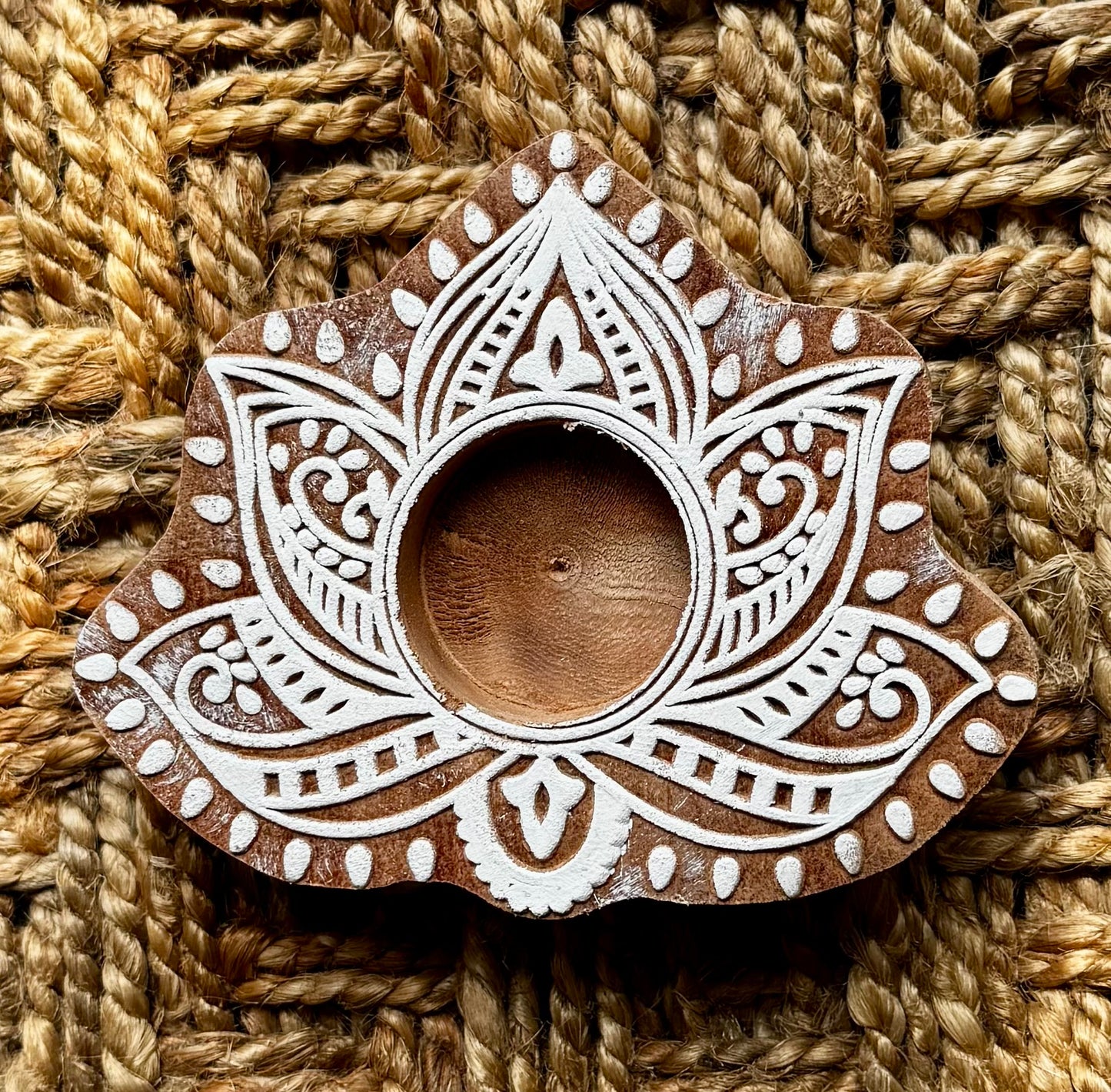 Decorative hand engraved wooden tealight holder in lotus shape with white patterns on a woven background