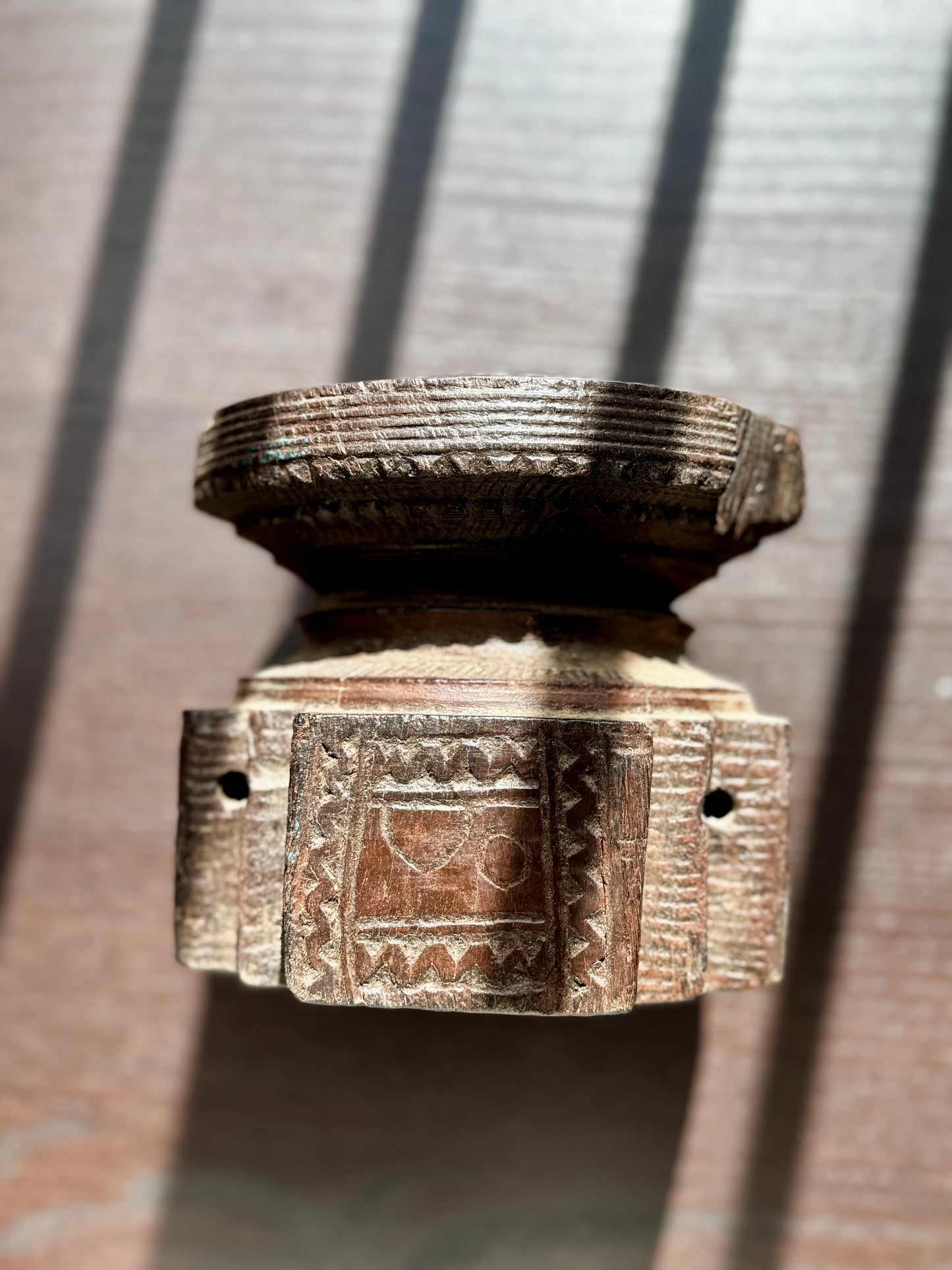 Decorative wood candle holder on its side with intricate designs on a textured surface