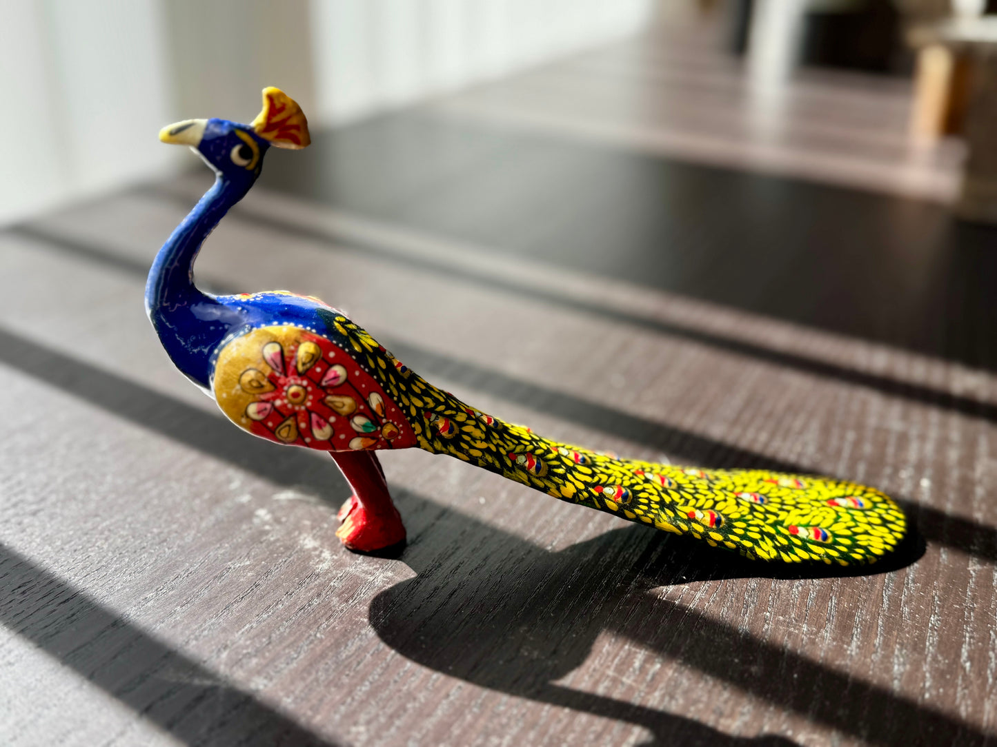 Colorful peacock figurine on a textured surface with a blurred background