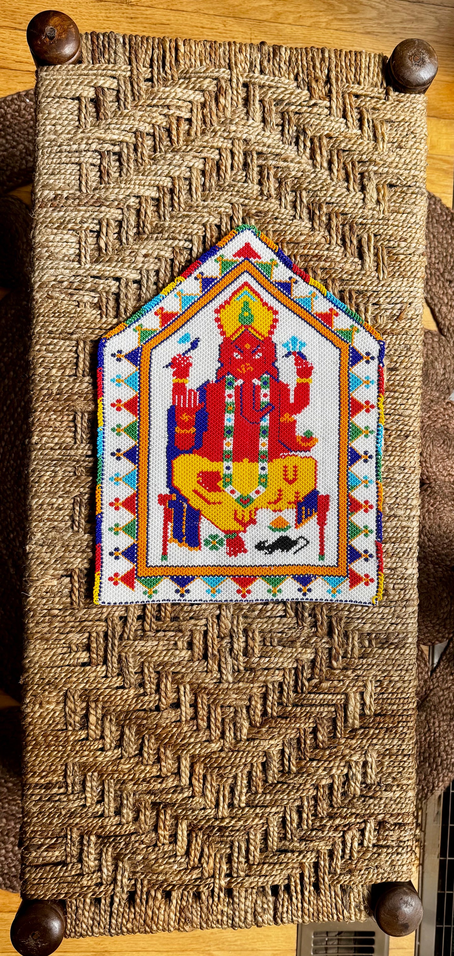 Decorative Motikaam - strung Pearl work Ganesha wall hanging with colorful design on a textured fabric background