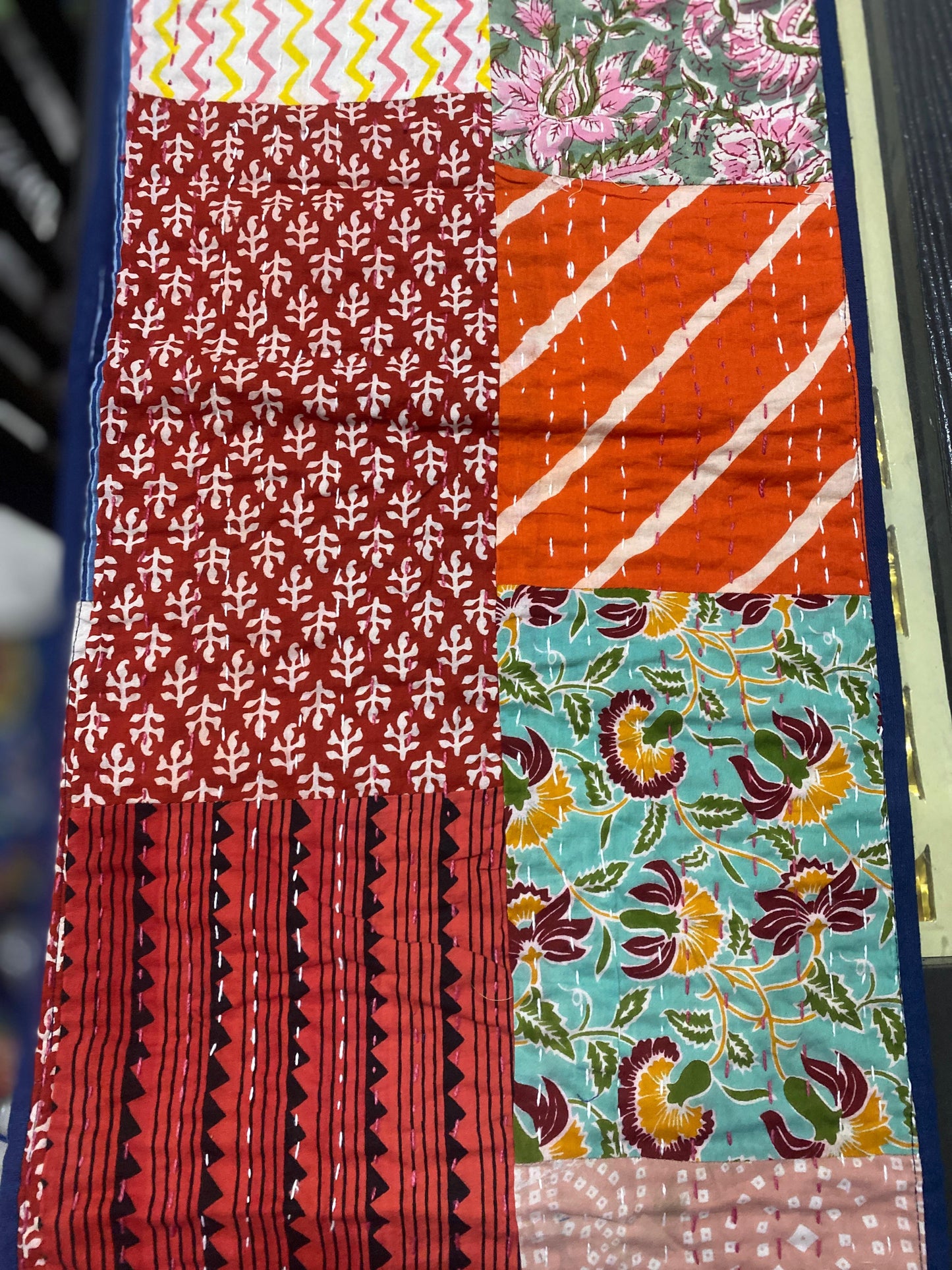 One side of Patchwork Kantha work table runner with various patterns and colors on a blue background