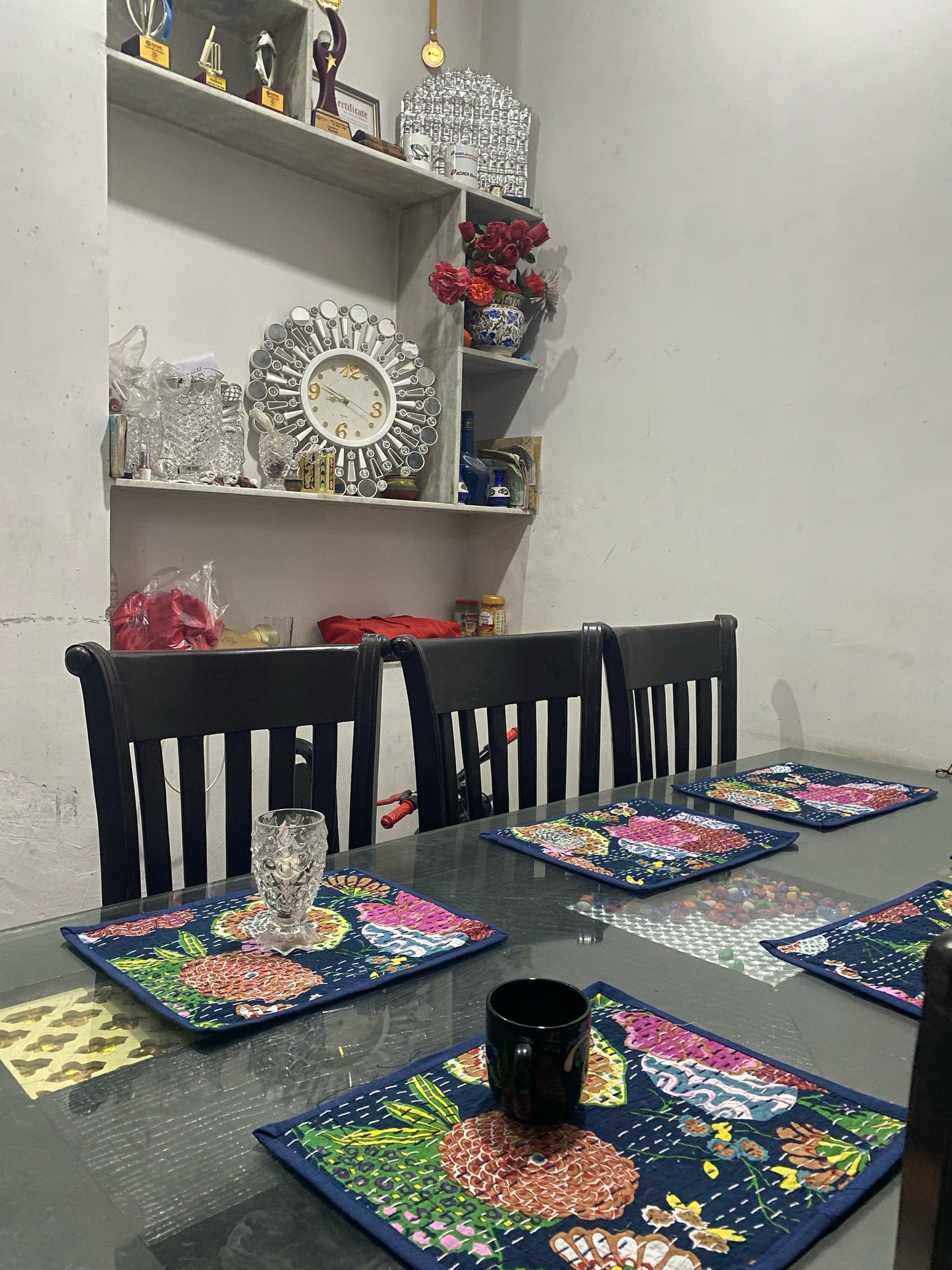 Dining table set with colorful placemats and chairs against a white wall.