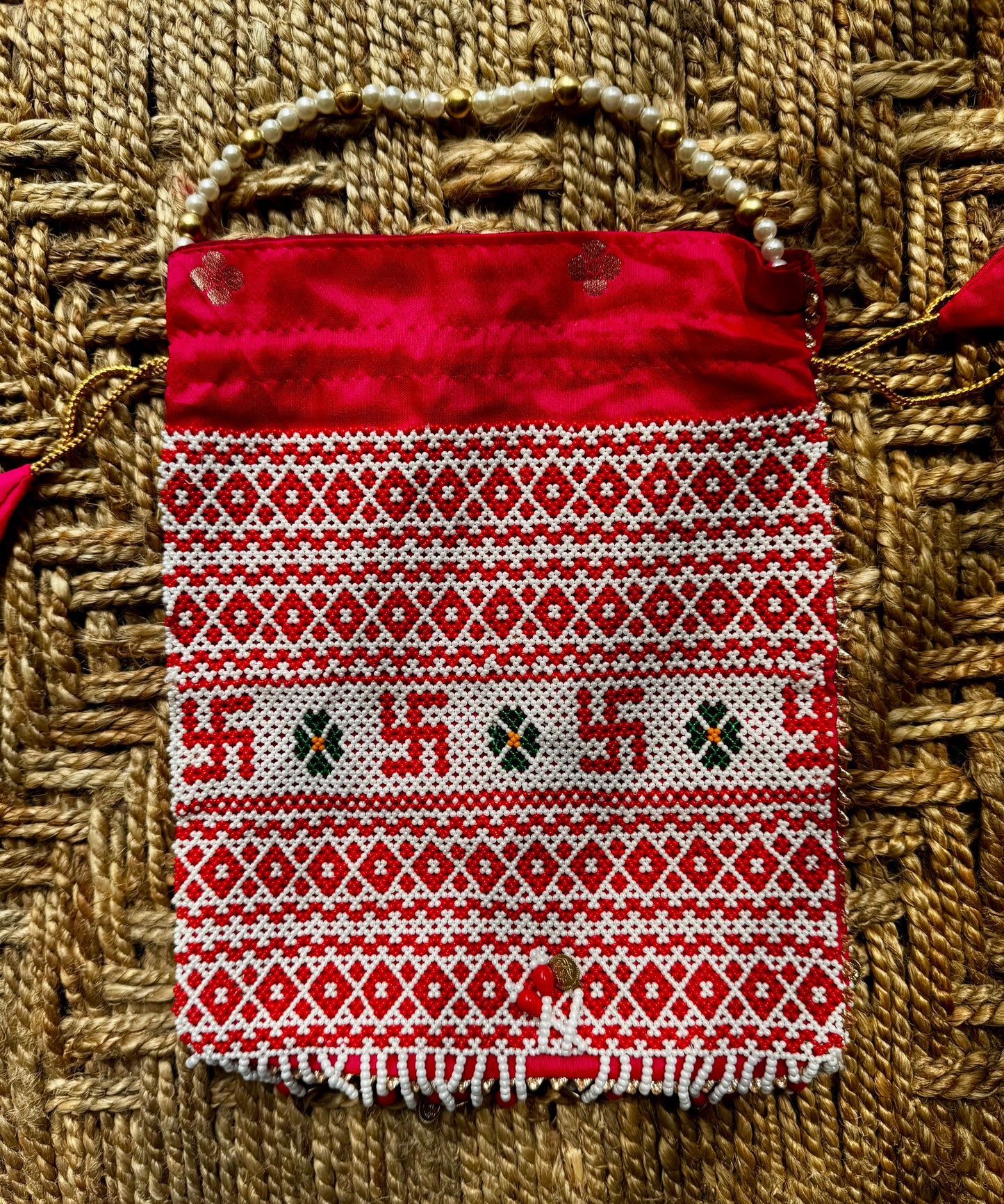 Red and white patterned pouch with decorative pearl work on a woven background
