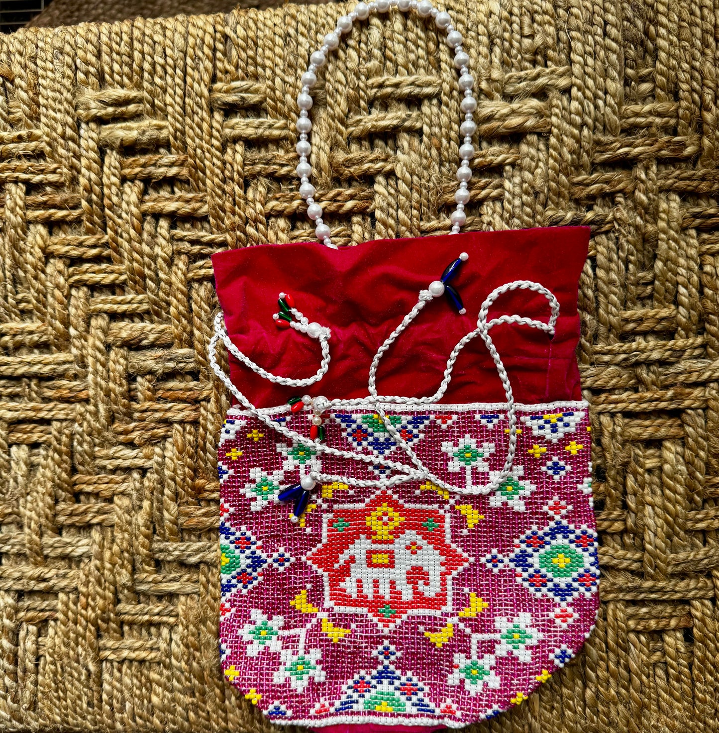 Decorative red bag/batwa/potli with intricate Pearl work on a textured woven surface