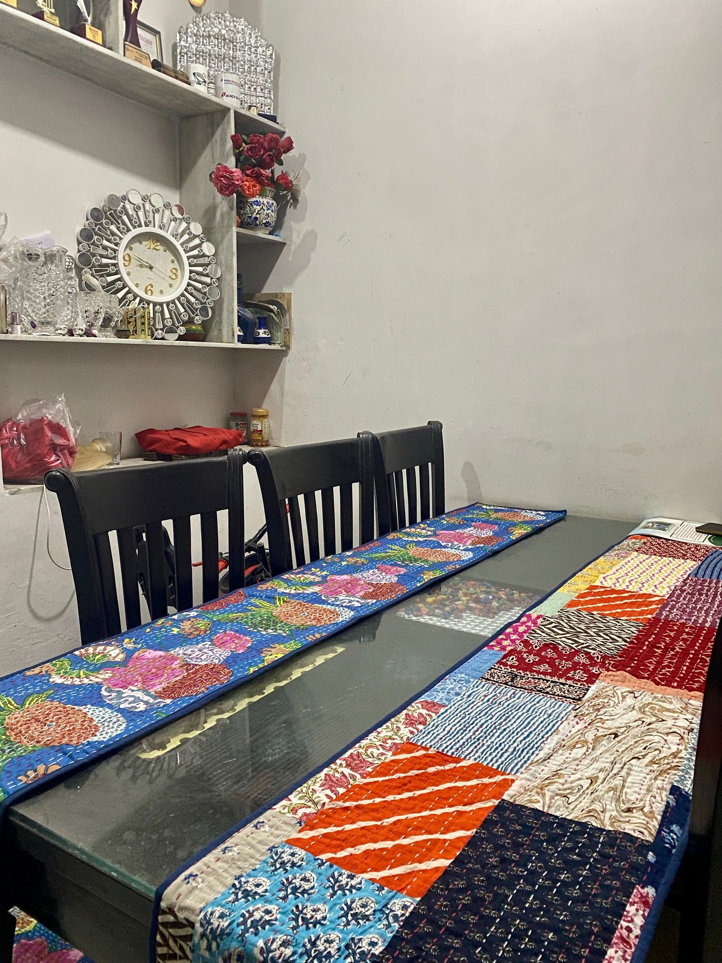 Dining table with a colorful Kantha work reversible table runner and chairs against a white wall.