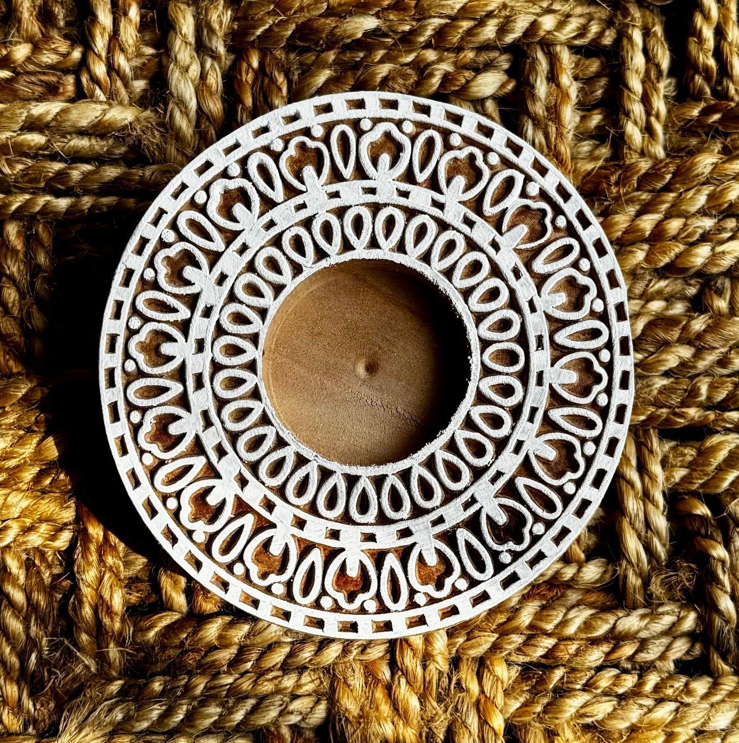 Decorative white circular hand engraved wood tea light holder with intricate patterns on a textured brown background