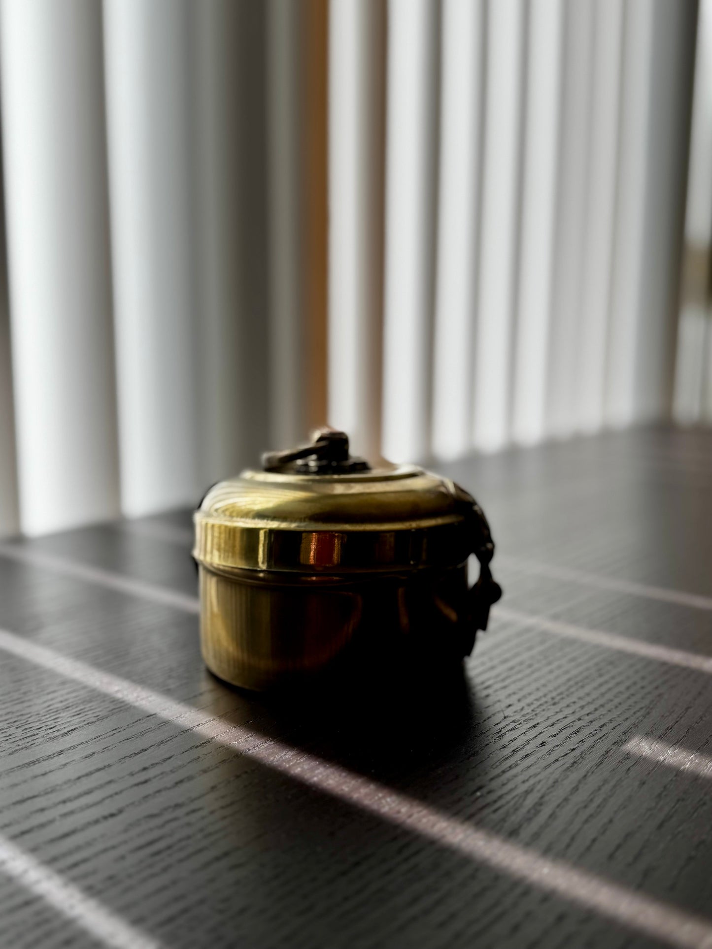 Brass container on a dark surface with light filtering through blinds in the background