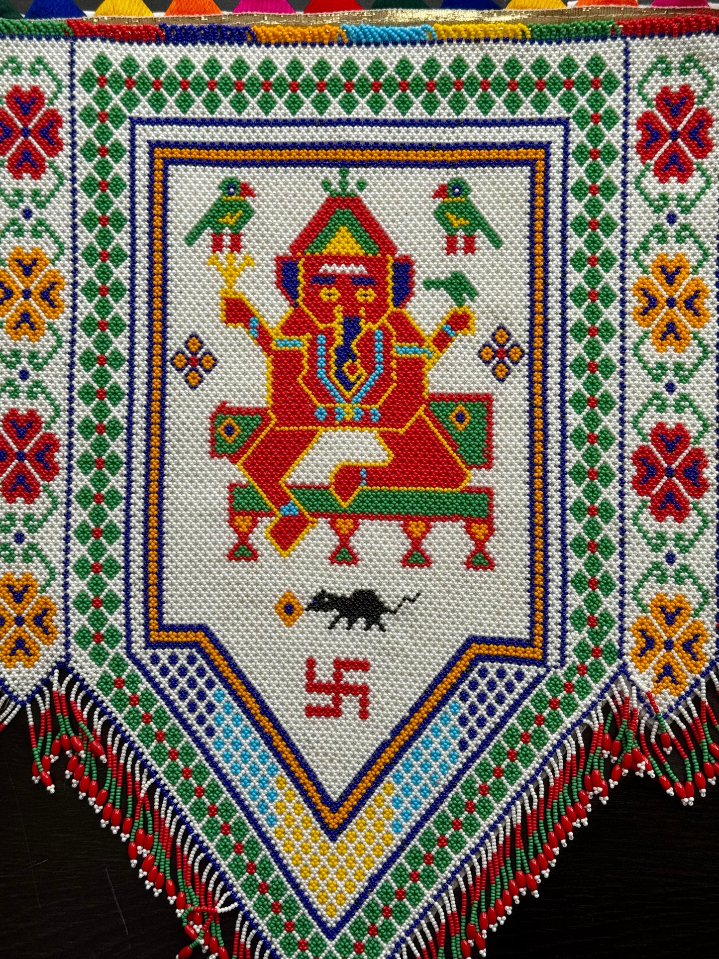 Decorative Motikaam wall hanging - strung pearls art with colorful patterns and fring on a black backgroun Colorful embroidered design with a central figure and geometric patterns