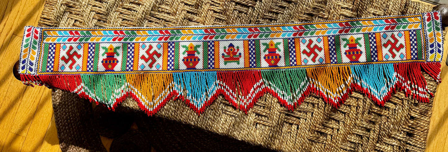 Decorative Motikaam - strung Pearl work wall hanging with colorful design on a textured fabric background. Colorful beaded border with geometric patterns on a woven background