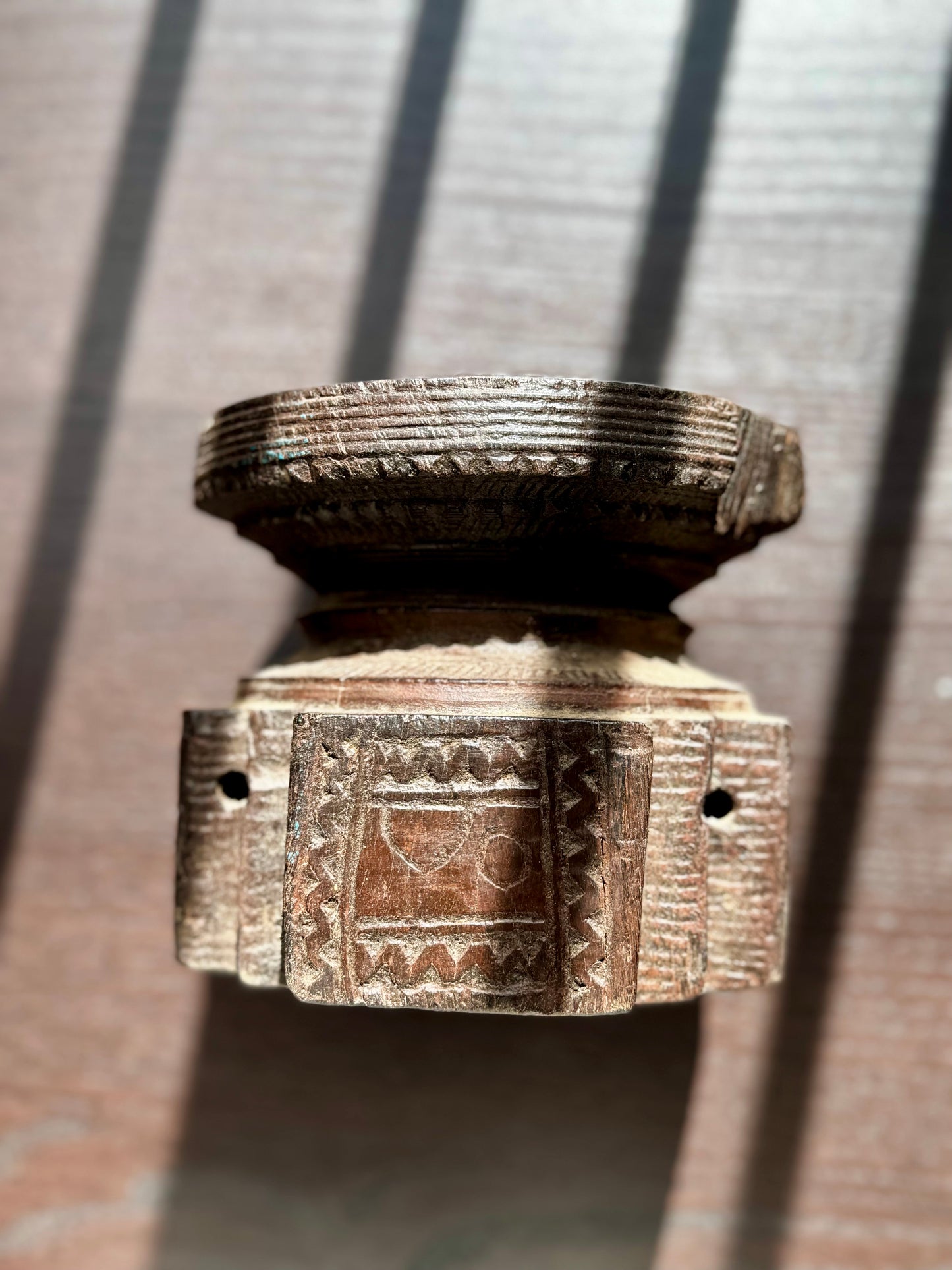 Decorative wood candle holder on its side with intricate designs on a textured surface