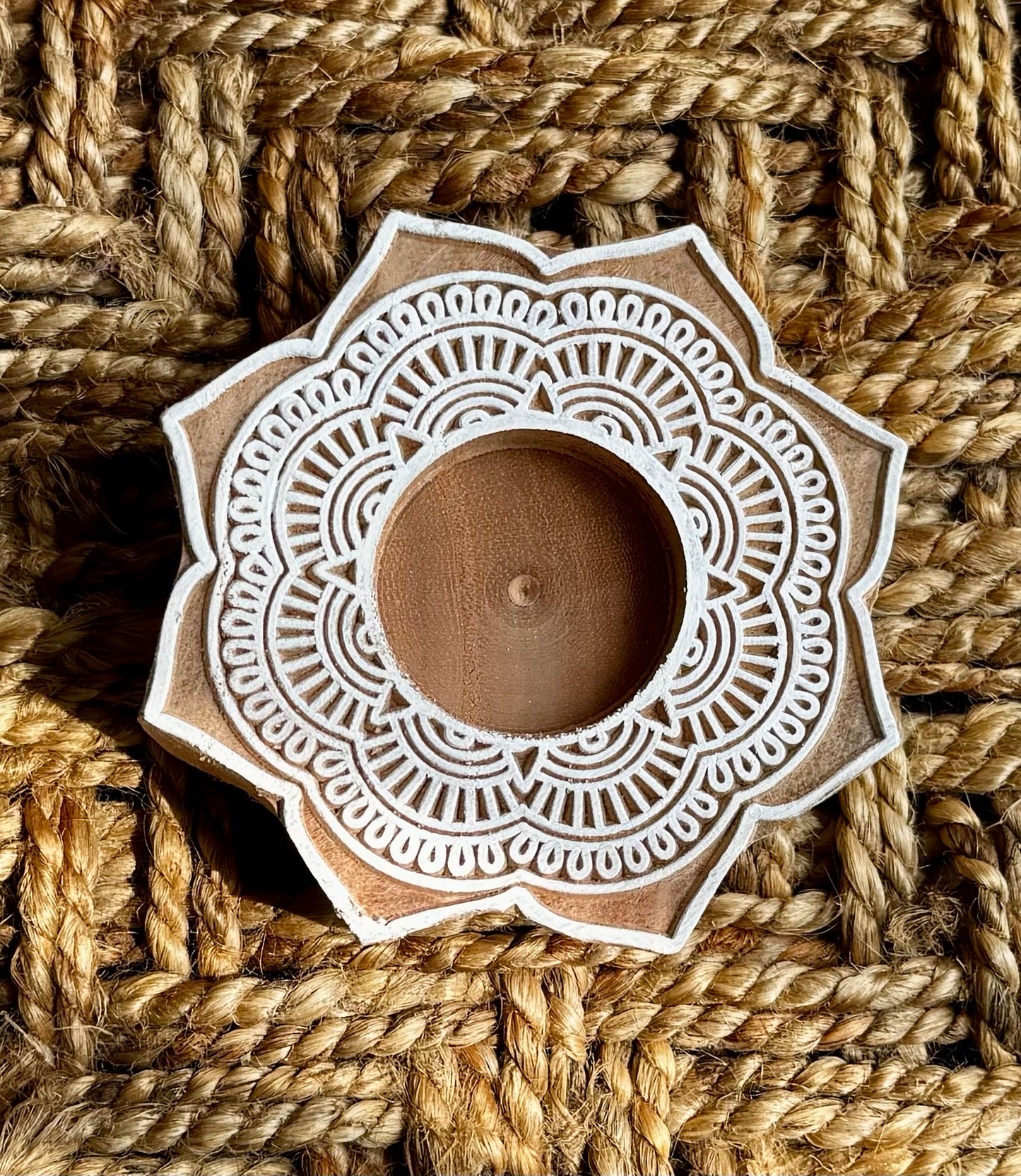 Decorative hand engraved wood tea light holder with intricate white patterns on a woven brown background