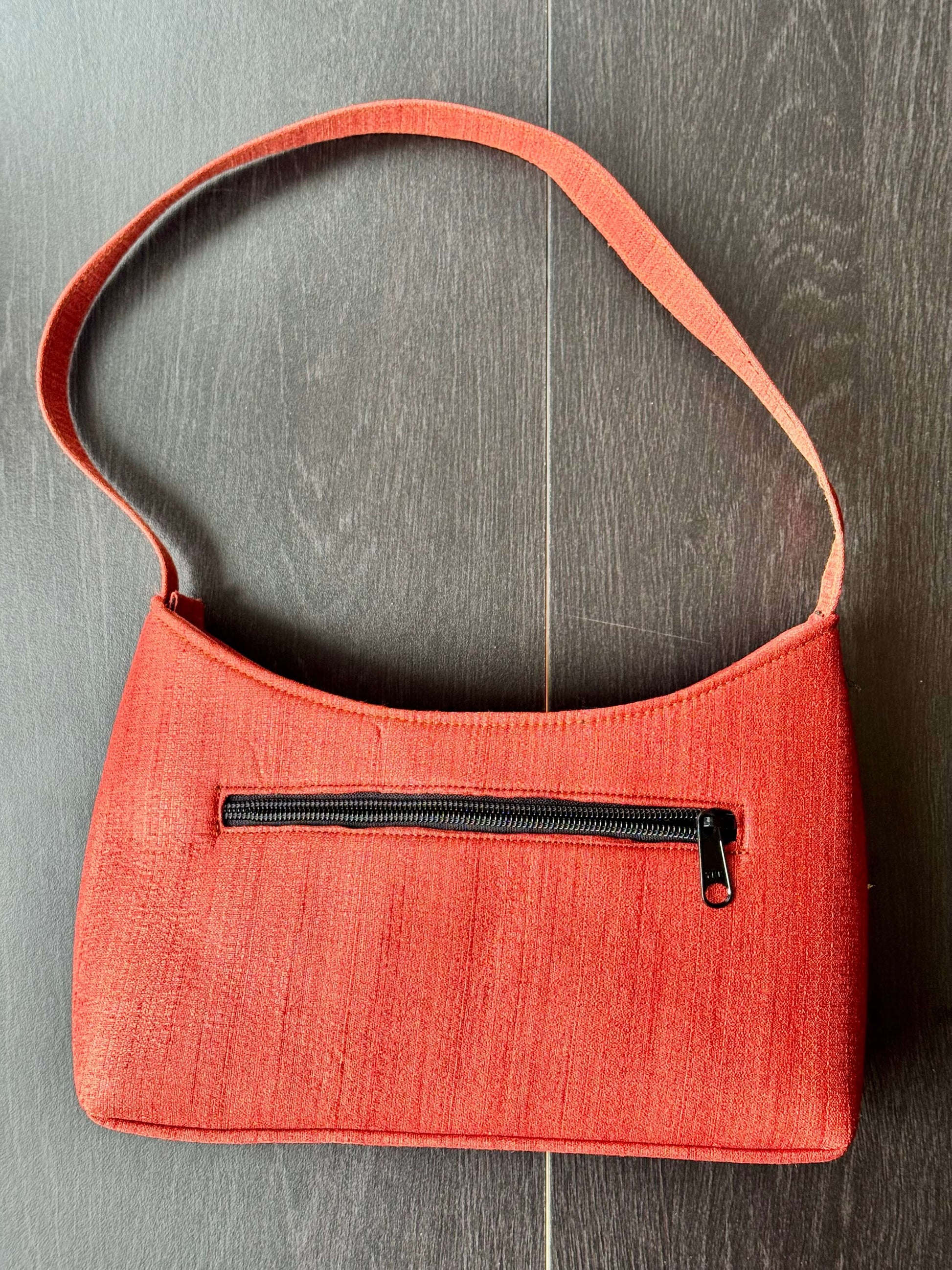Coral handbag with a black zipper on a wooden surface