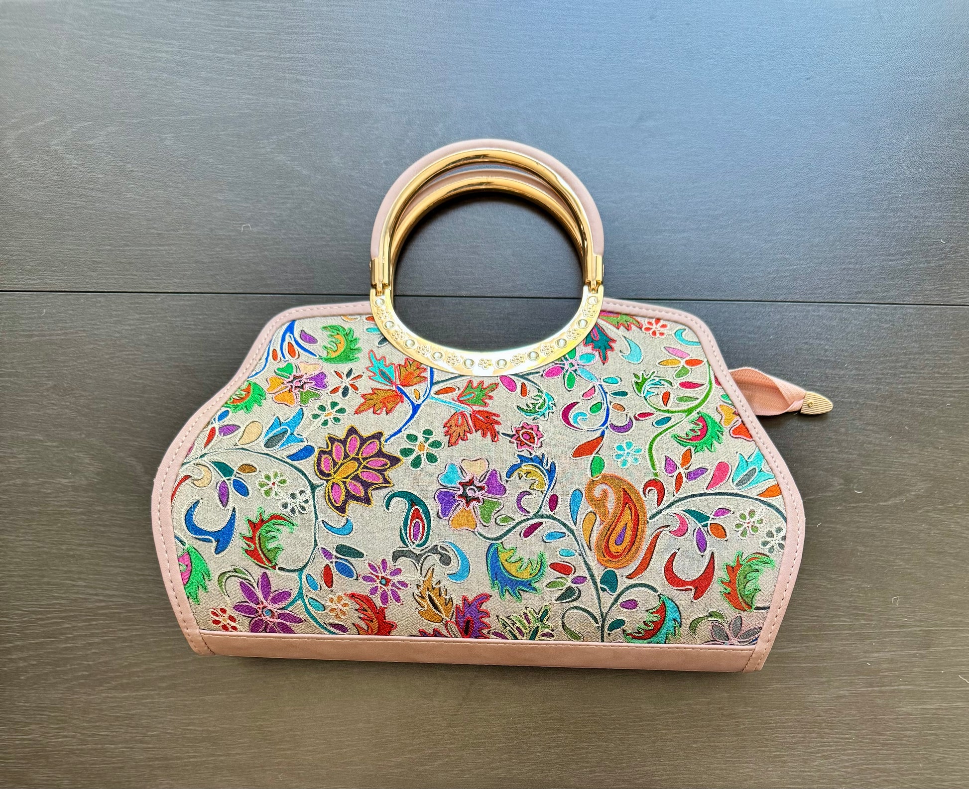 Colorful floral handbag with intricate Kashmiri Kashida work and a gold handle on a wooden surface