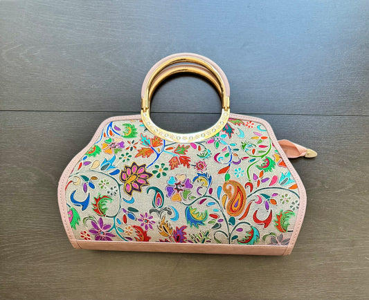 Colorful floral handbag with intricate Kashmiri Kashida work and a gold handle on a wooden surface