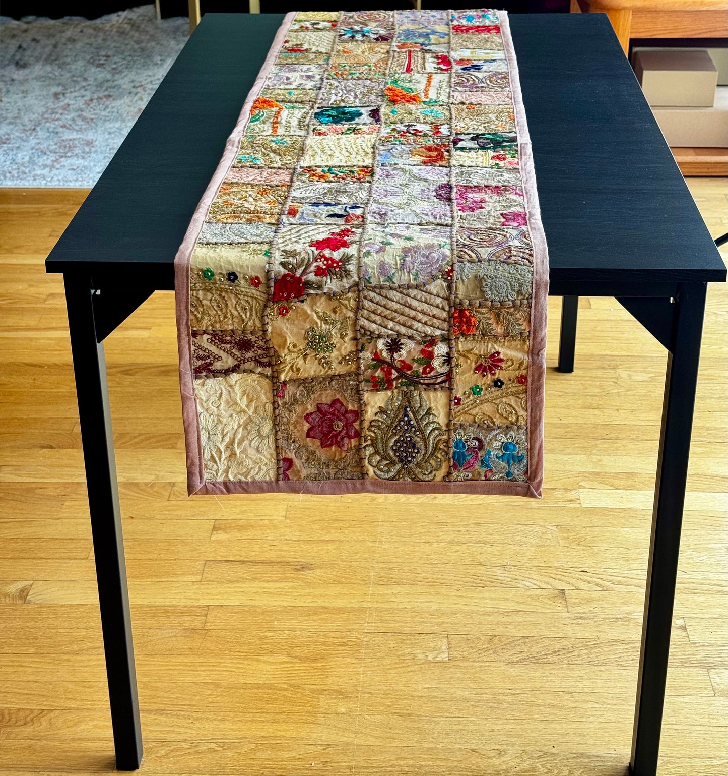 Khambhadia Patchwork table runner on a black table with a wooden floor background