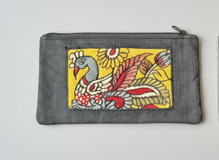 Close-up of a hand-painted makeup pouch with traditional Kalamkari art design featuring a bird and floral motifs in bright colors on a yellow background.
