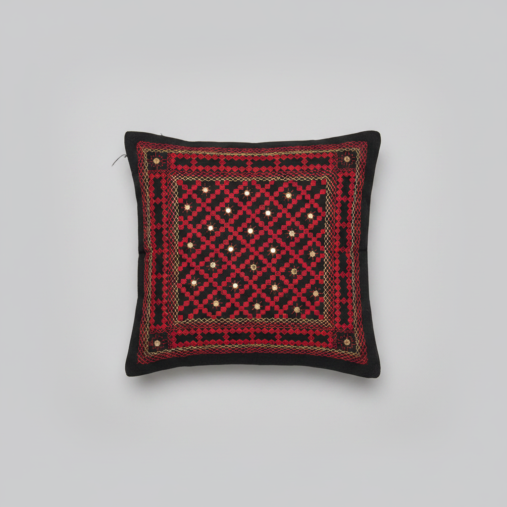 Decorative pillow with red and black Kutchi embroidery pattern on a gray background