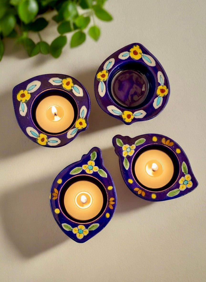 Four purple Jaipur Blue pottery Diwali lamps with floral designs on a beige background.