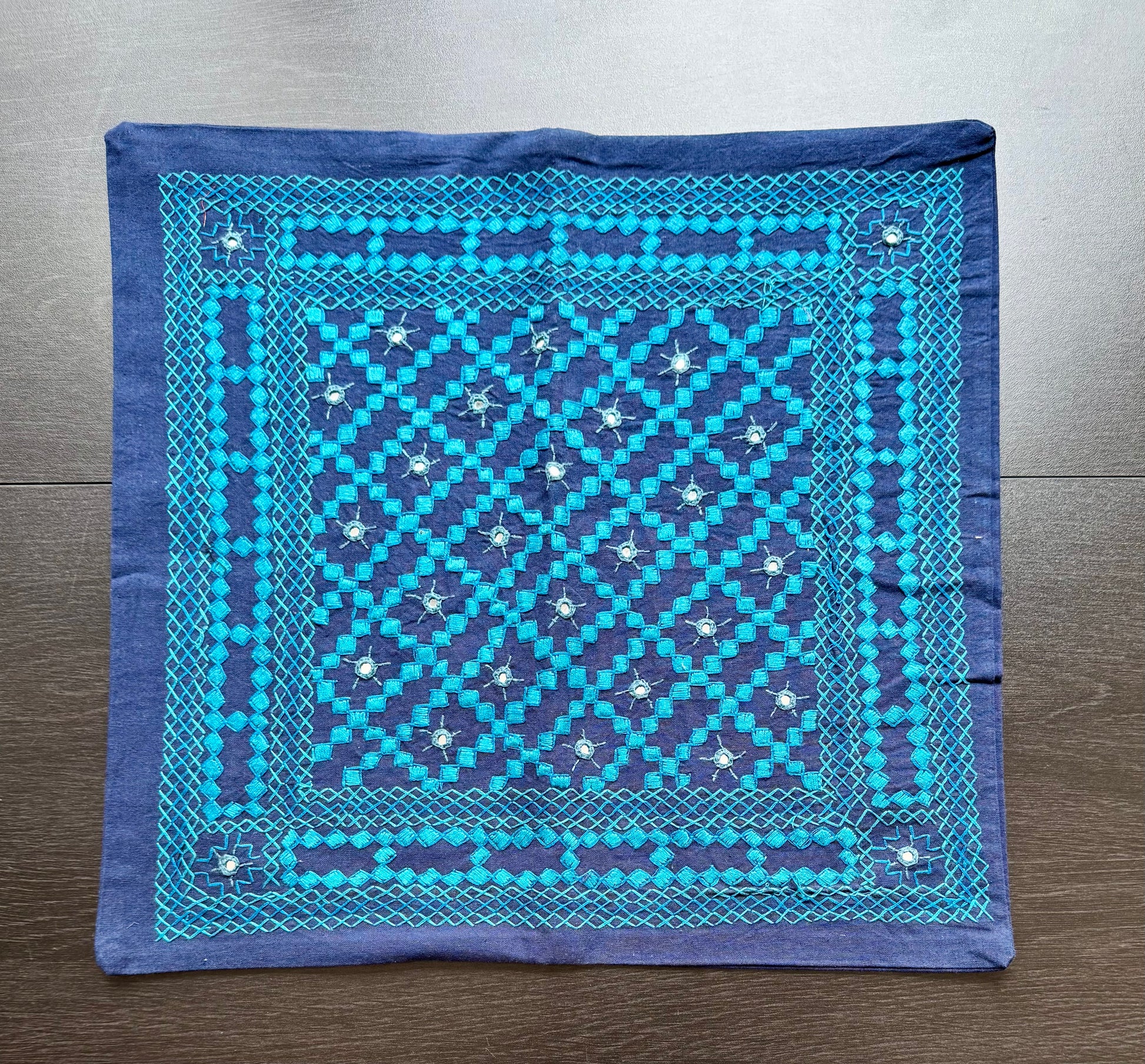 Blue cushion cover with intricate white Kutchi embroidery patterns on a wooden surface
