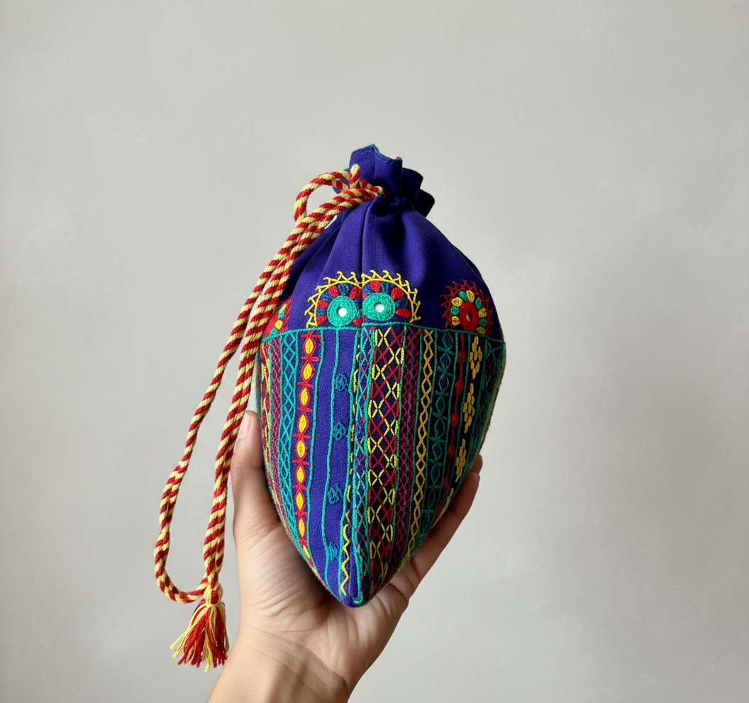 Hand holding a colorful embroidered fabric pouch against a plain background
