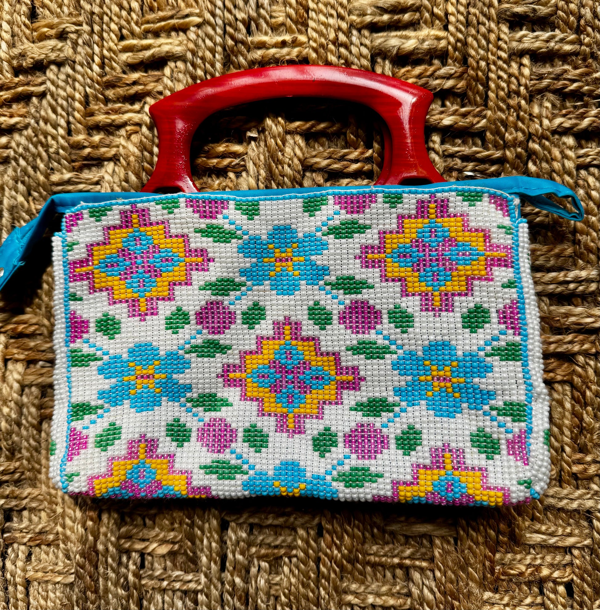 Decorative Motikaam - strung Pearl work handbag clutch with colorful design on a textured fabric background Handmade cross-stitched bag with colorful floral patterns on a woven surface