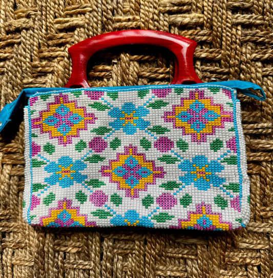 Decorative Motikaam - strung Pearl work handbag clutch with colorful design on a textured fabric background Handmade cross-stitched bag with colorful floral patterns on a woven surface