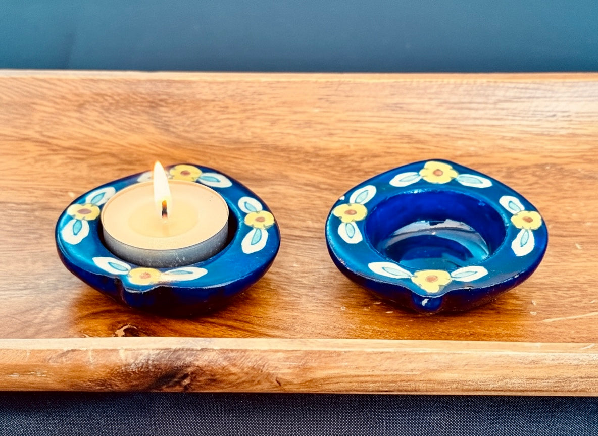 Two Jaipur blue pottery tea light holders with floral designs on a wooden surface.
