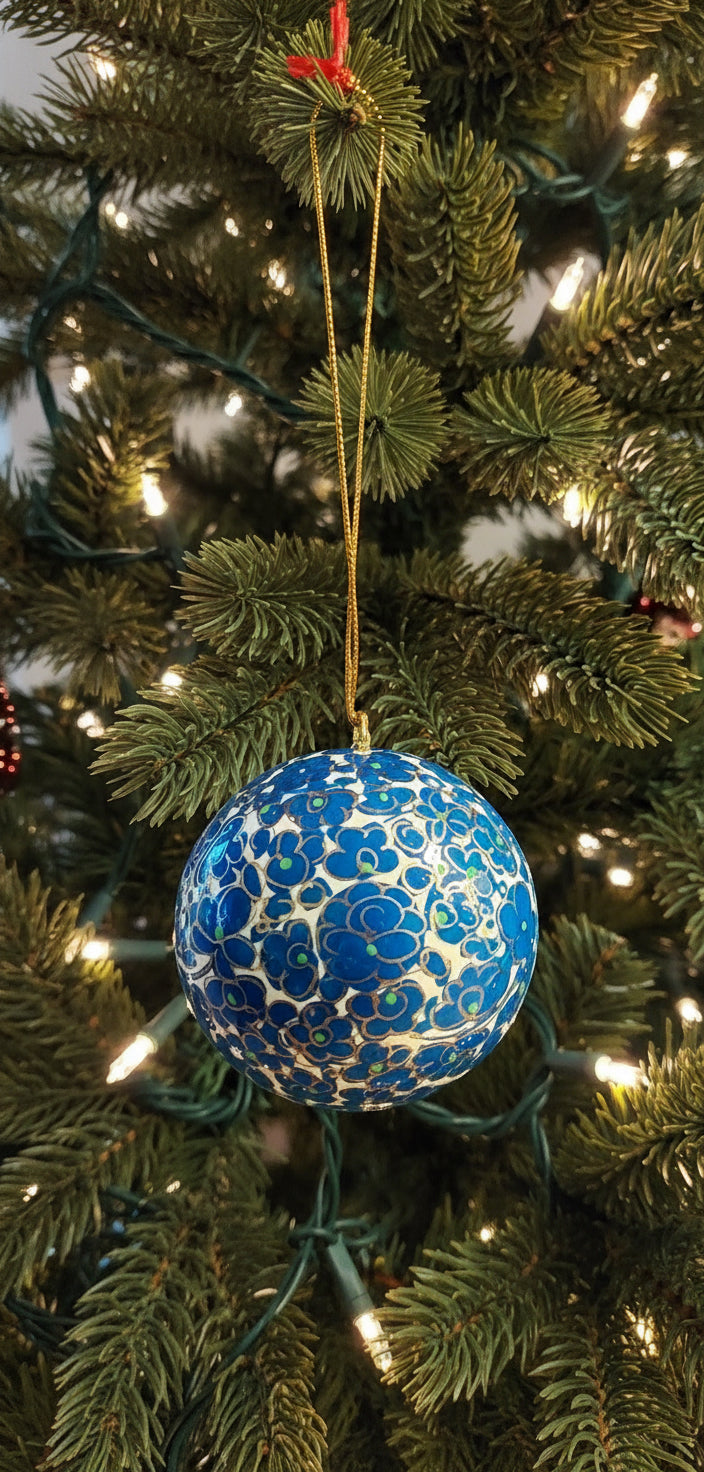 Blue floral ornament with gold accents on a string, held by a hand against a neutral background.