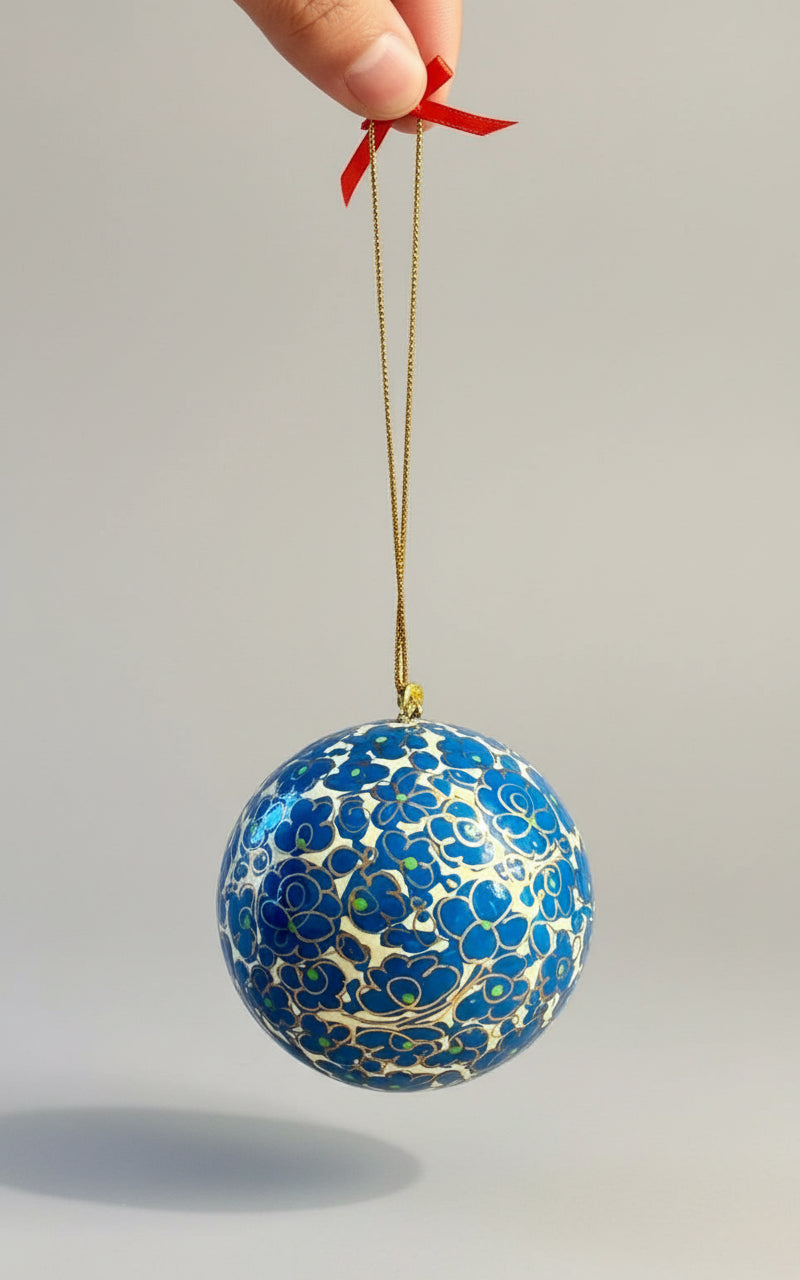 Blue decorative ball with gold patterns hanging from a string against a neutral background