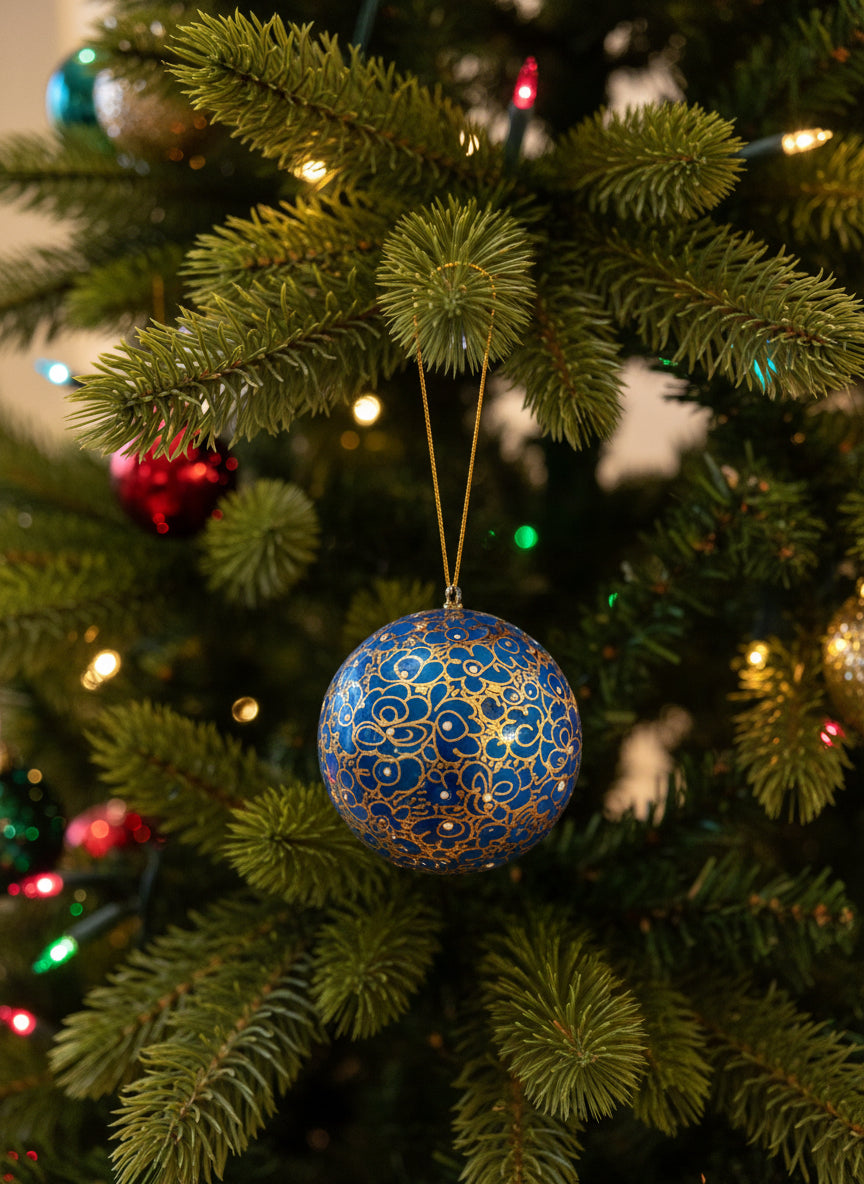 A decorative purple design on ivory ball hanging on the branch of Christmas tree