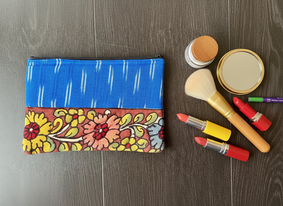 Close-up of a hand-painted makeup pouch with traditional Kalamkari art design featuring a bird and floral motifs in bright colors on a yellow background.