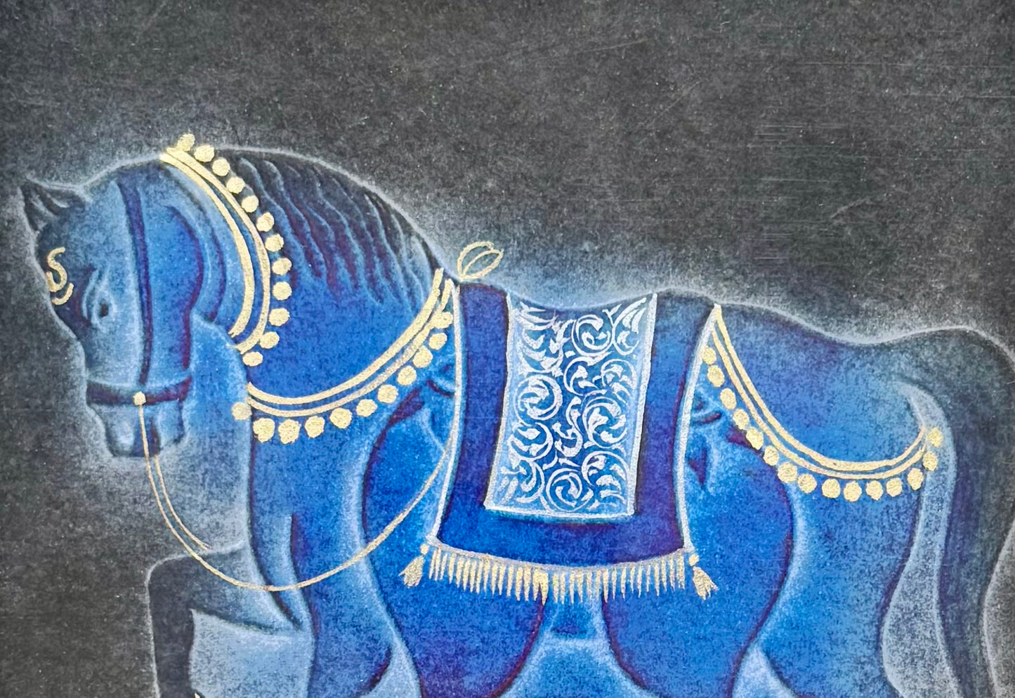 Close up of nail drawn artwork of a blue horse with gold detailing on a textured gray background