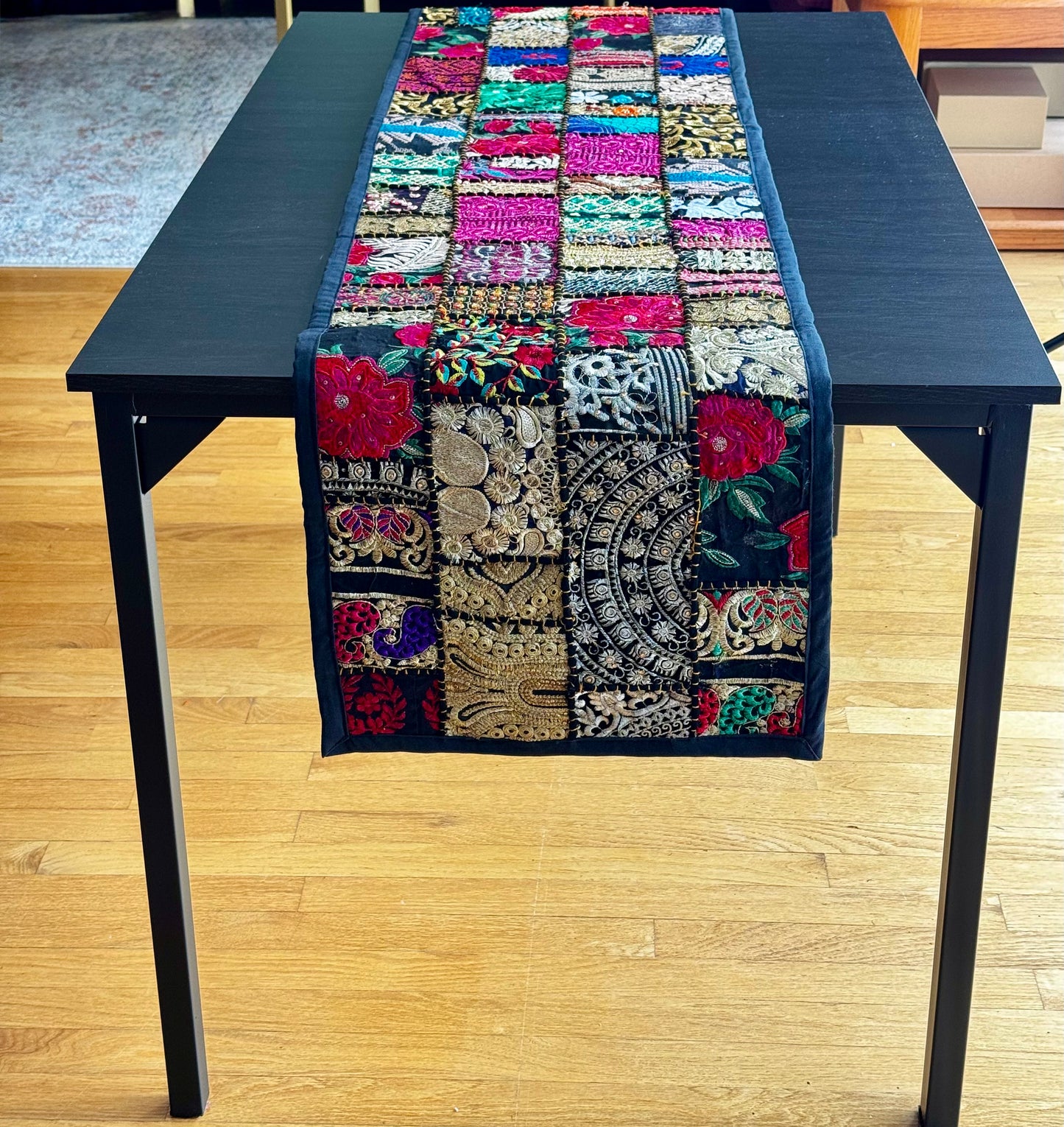 Colorful Khambhadia patchwork table runner on a black table with a wooden floor background