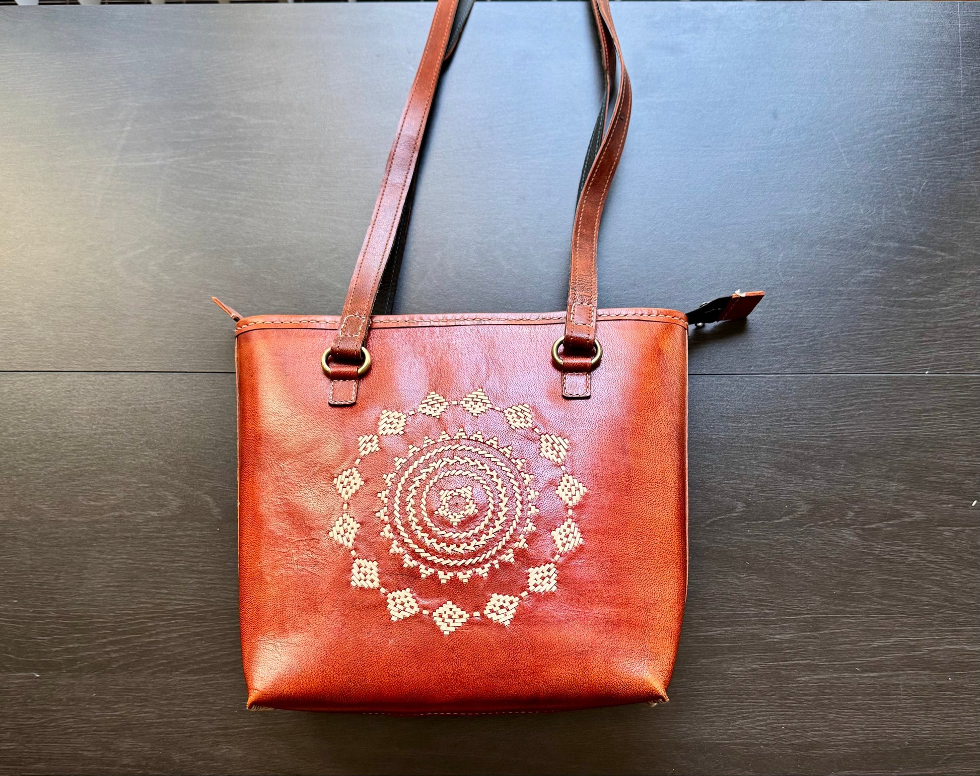 Brown Kutchi leather tote bag with a decorative pattern on a wooden surface