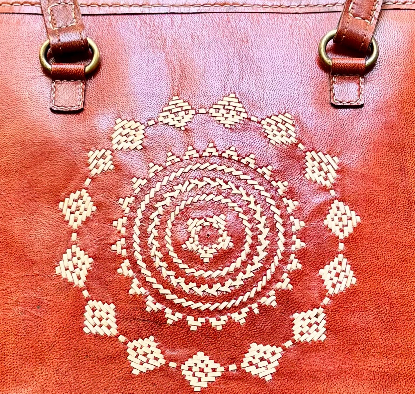 Brown leather tote bag with a decorative pattern on a wooden surface